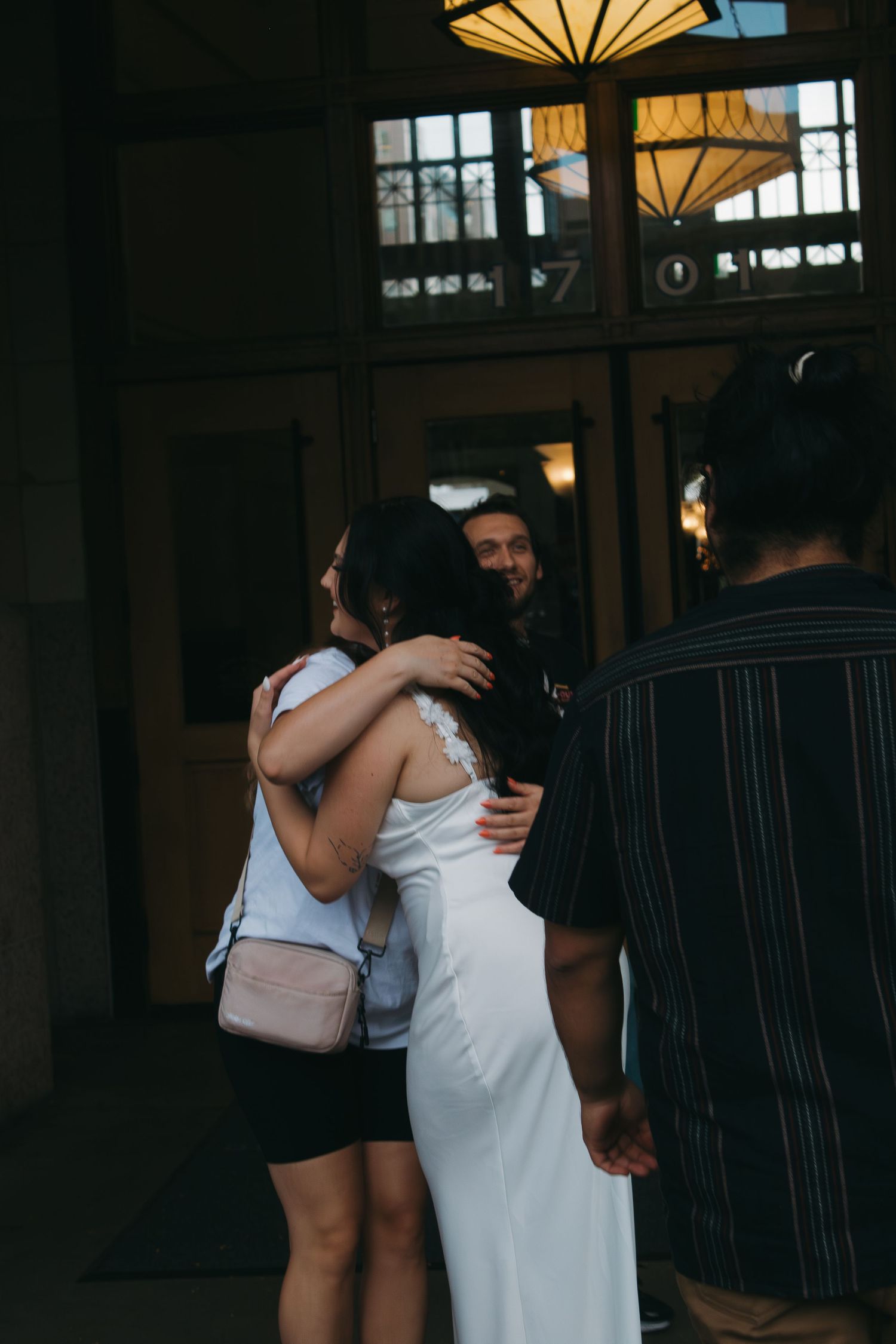 A group sharing warm embraces in a dimly lit indoor space with decorative lighting.