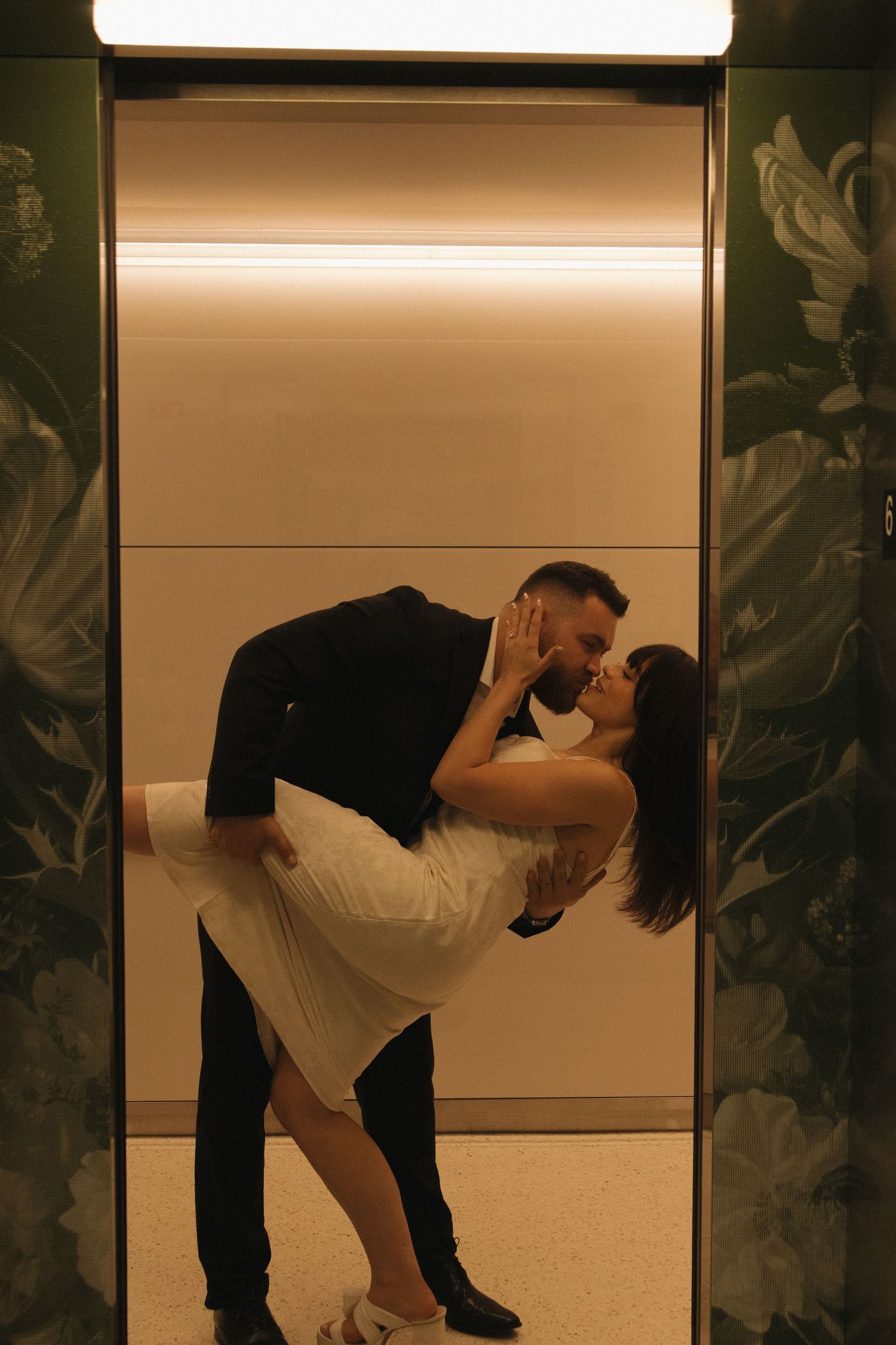 A dramatic dip pose between a couple in formal wear inside an elevator with patterned walls.
