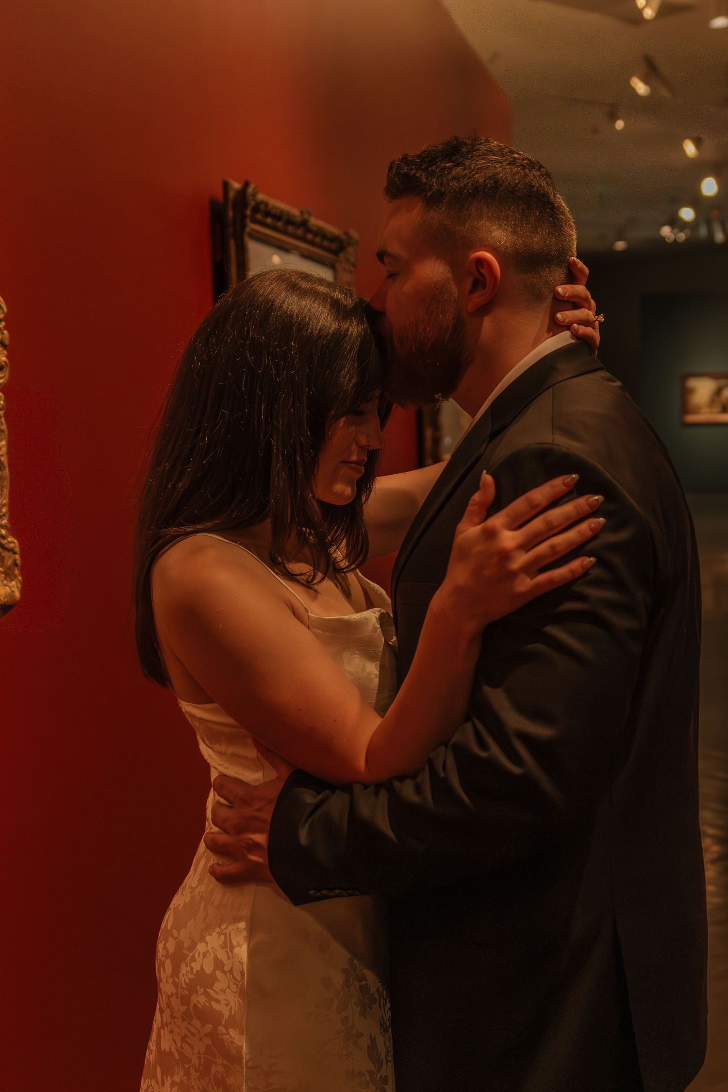 A couple shares an intimate dance moment in a dimly lit room with warm red lighting.