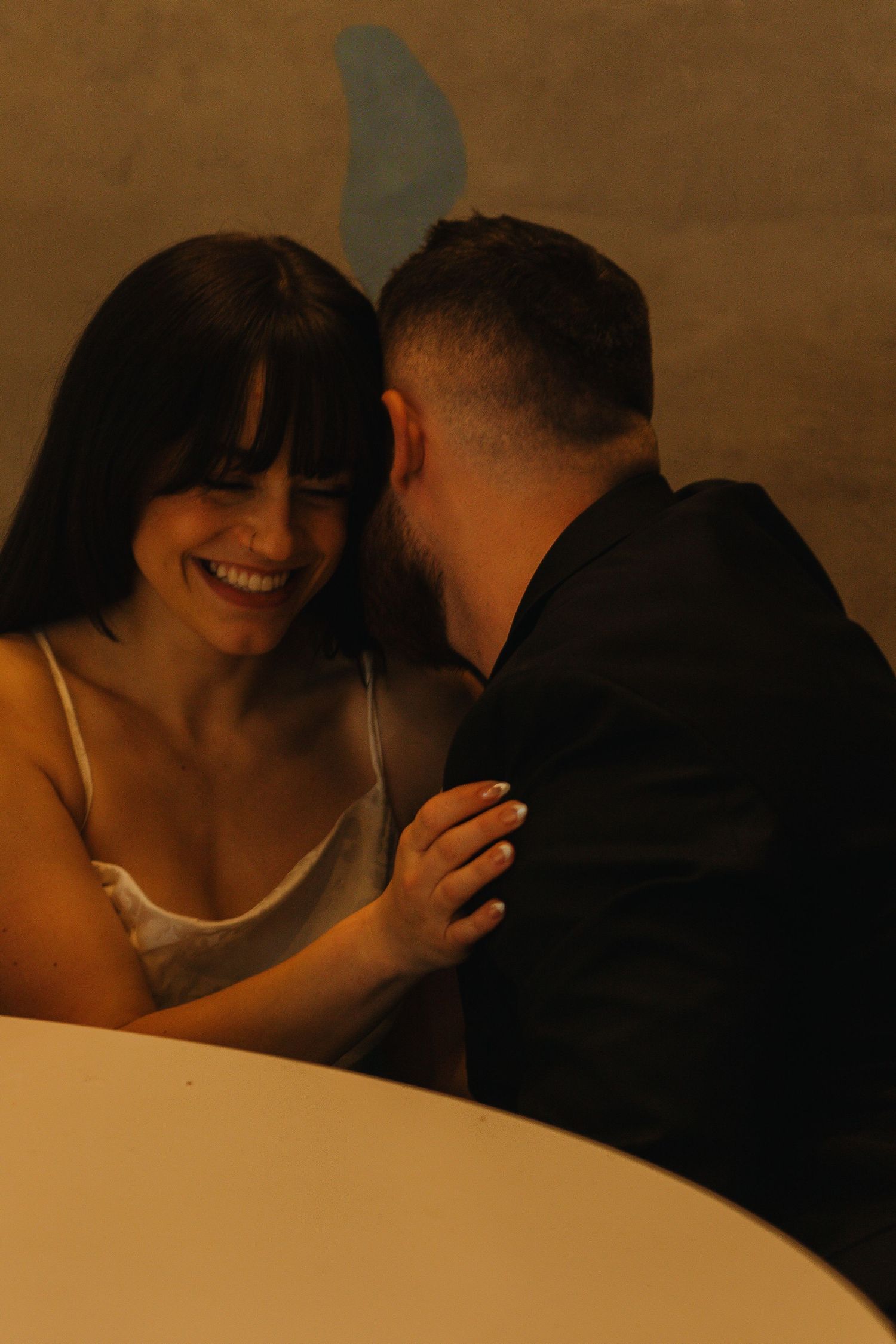 Intimate moment between couple captured in warm-toned lighting against curved wall.
