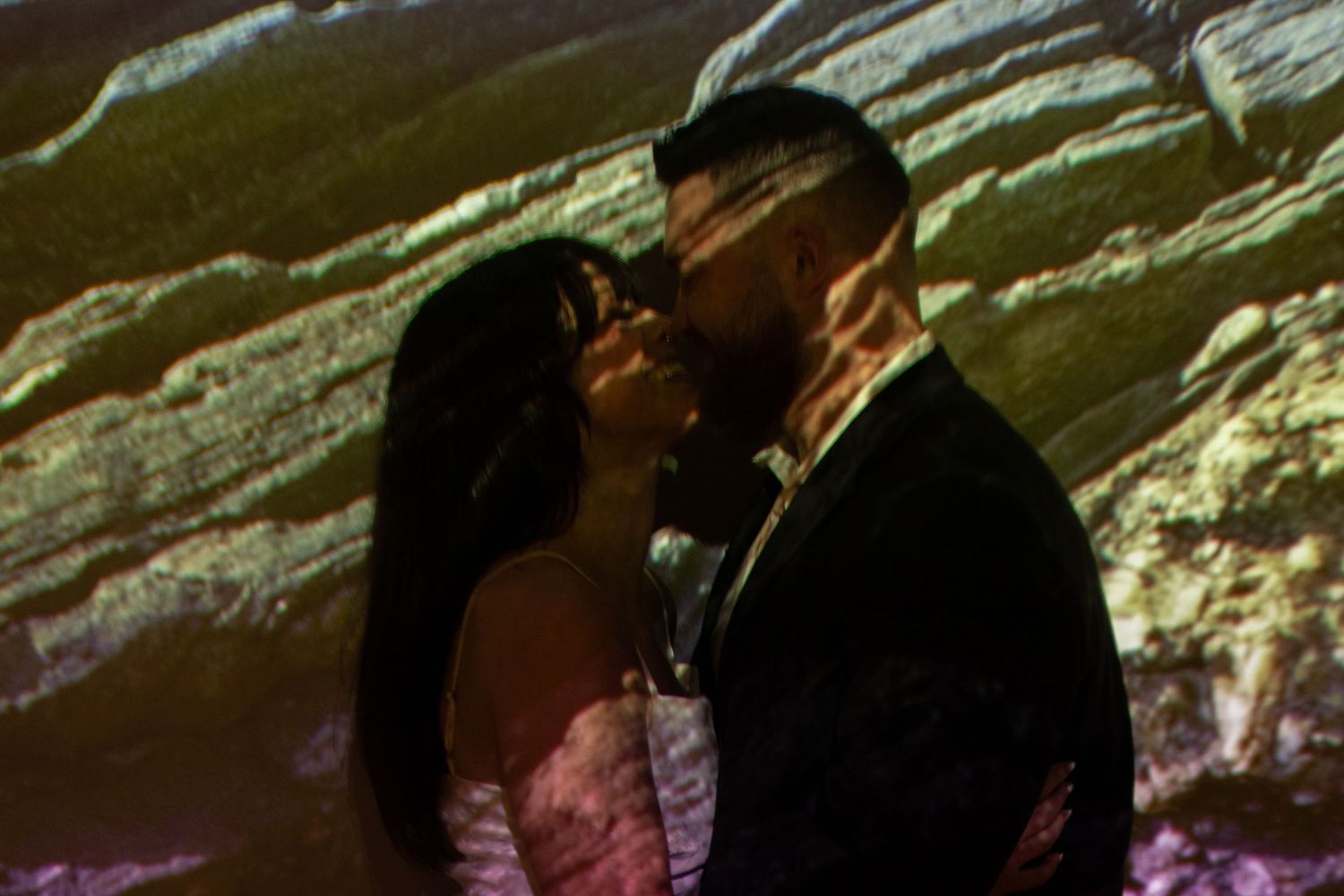 Silhouetted couple sharing intimate moment against colorful projected background.