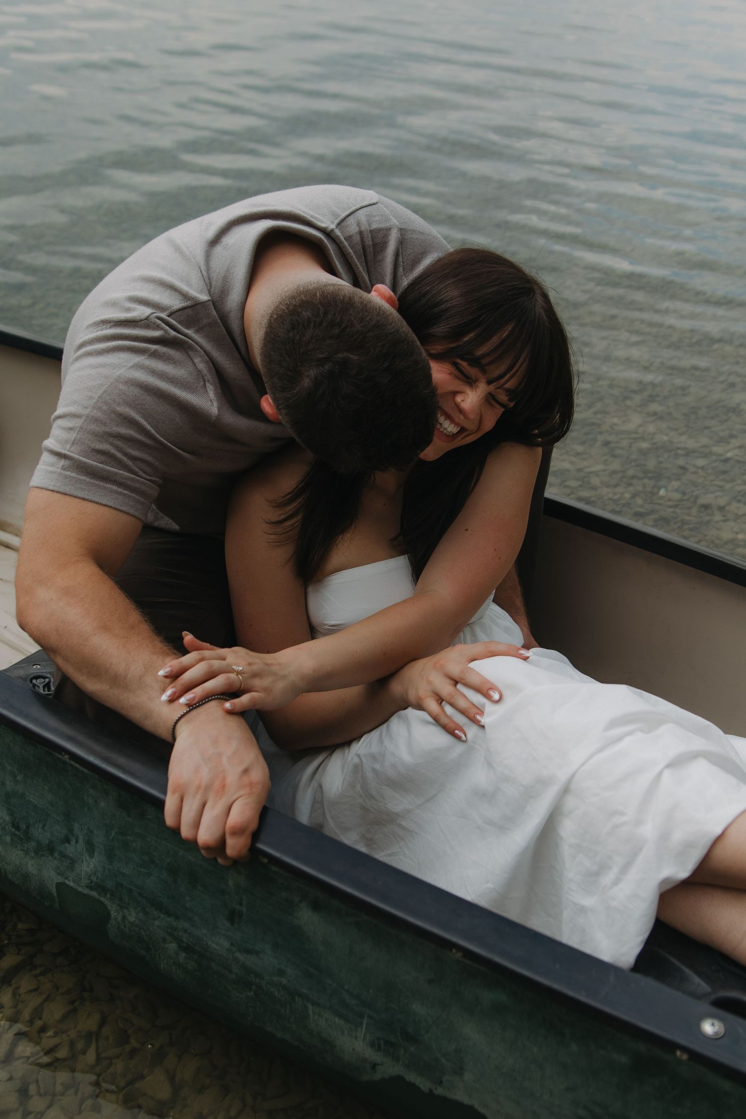 Couple in a close embrace laying on a dark surface near water.
