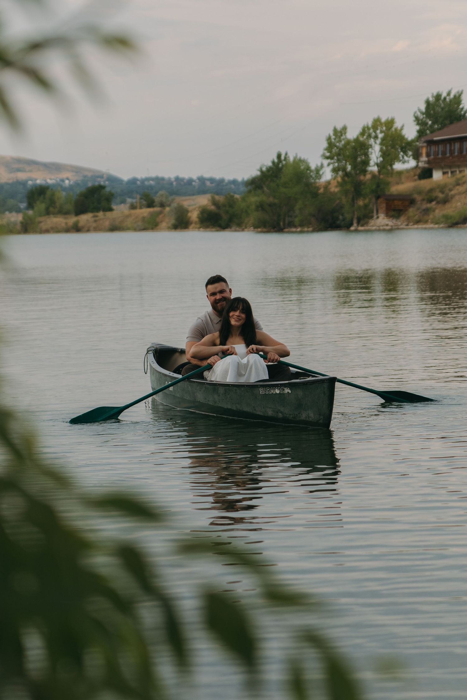 A romantic couple paddling together in a canoe on a serene lake at dusk.