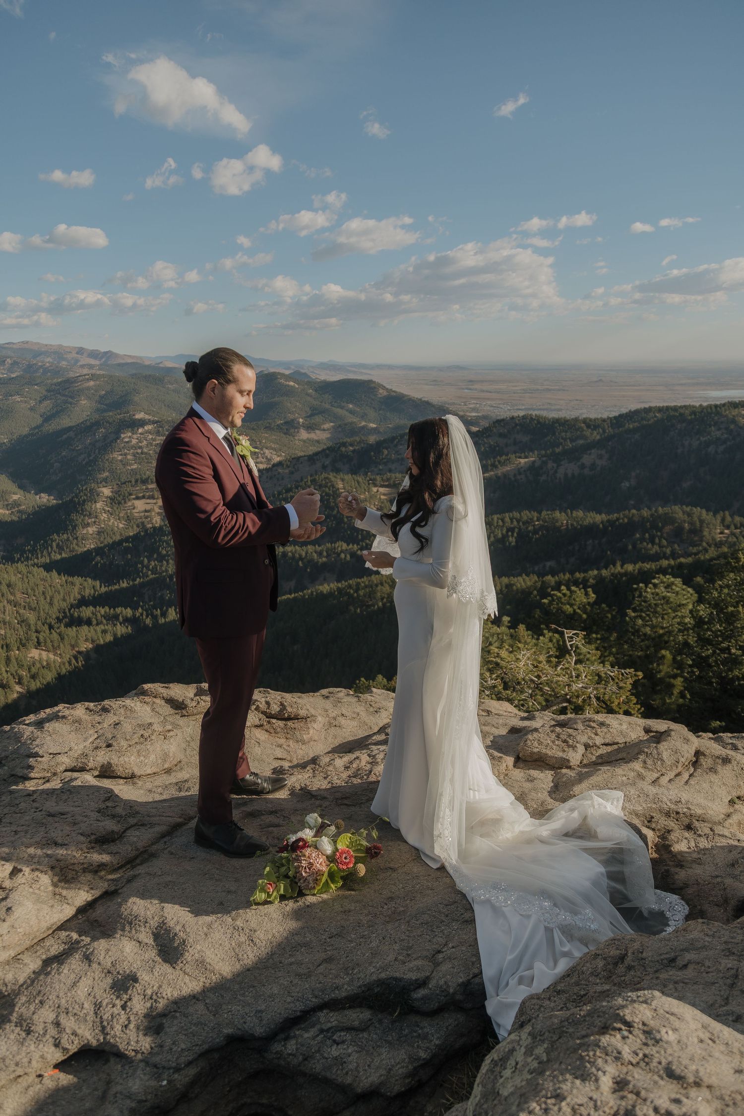 Bride and groom exchanging vows on rocky mountain summit with sweeping Colorado valley views below.