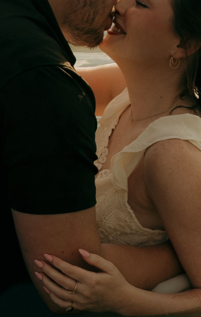 Couple sharing a romantic kiss, woman in lace dress with gold hoop earrings, man in black shirt, close-up intimate moment.