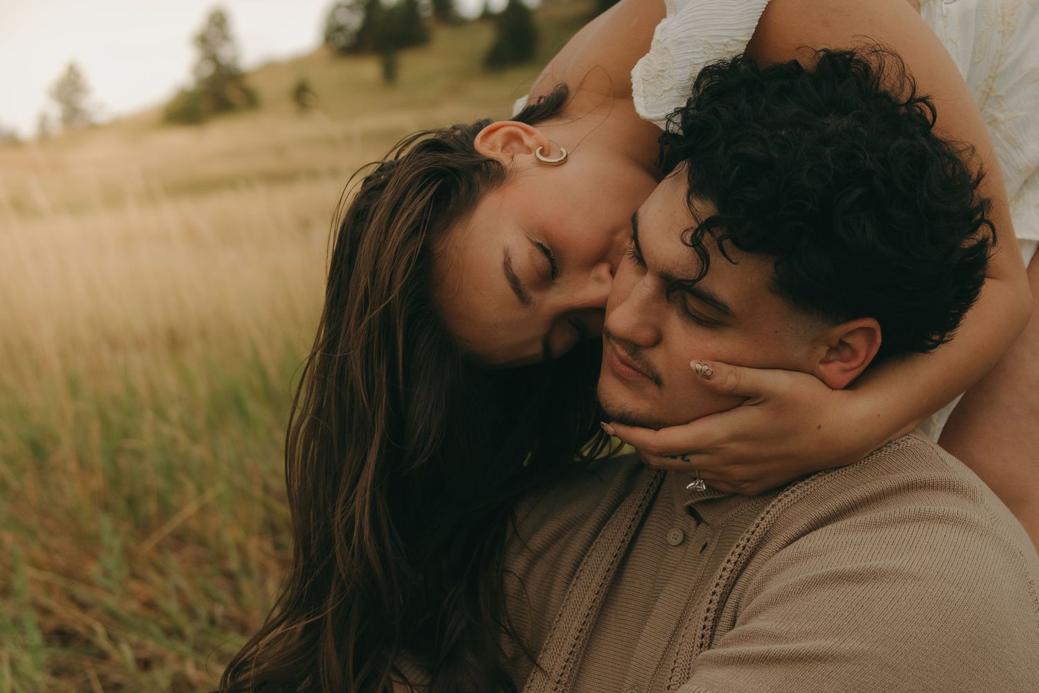 A tender moment as a couple sits close together in a sun-kissed golden field, faces touching.