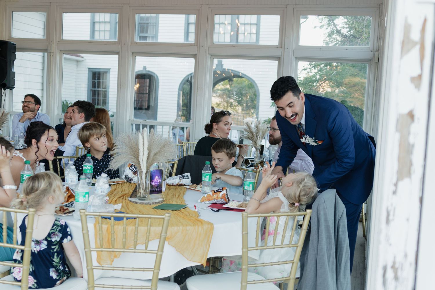 Wedding reception in bright sunlit room with string lights and large windows.