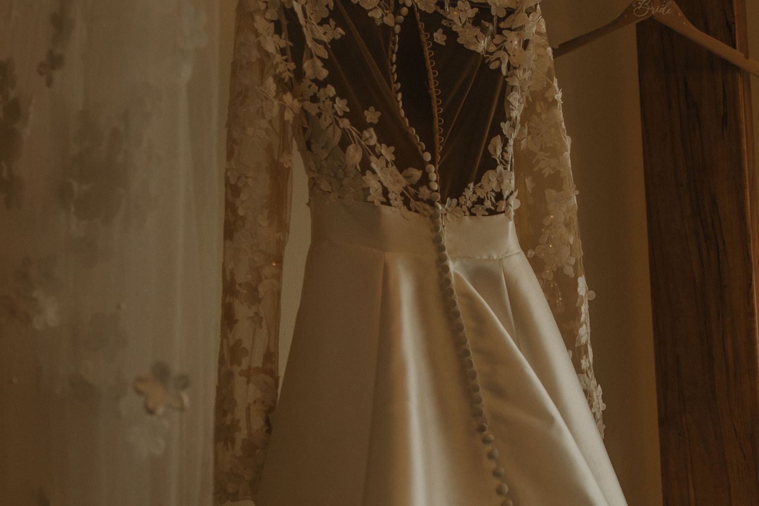 Three elegant vintage wedding dresses displayed on hangers in a rustic setting with warm lighting.