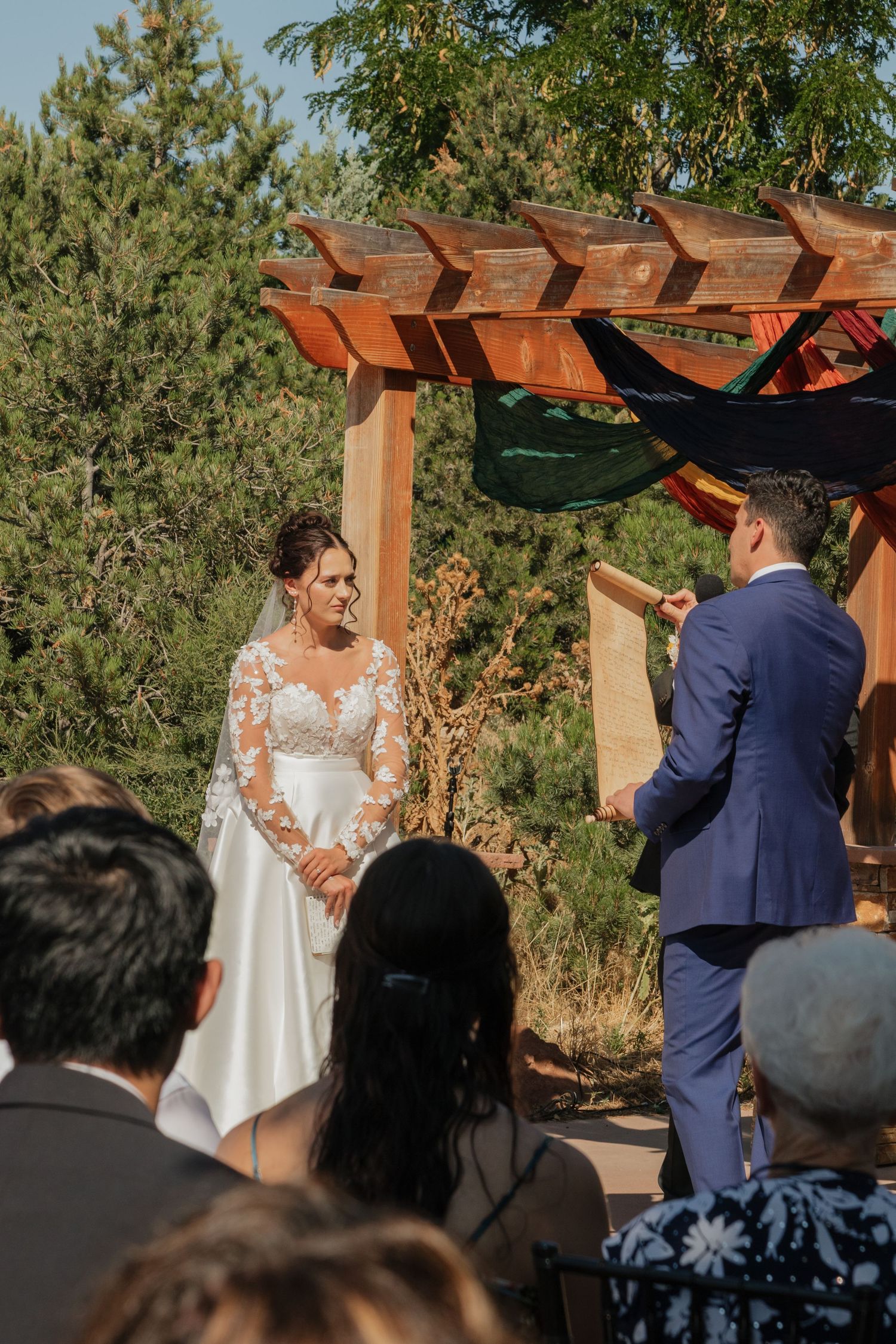 Outdoor wedding ceremony under a wooden pergola with mountain scenery.