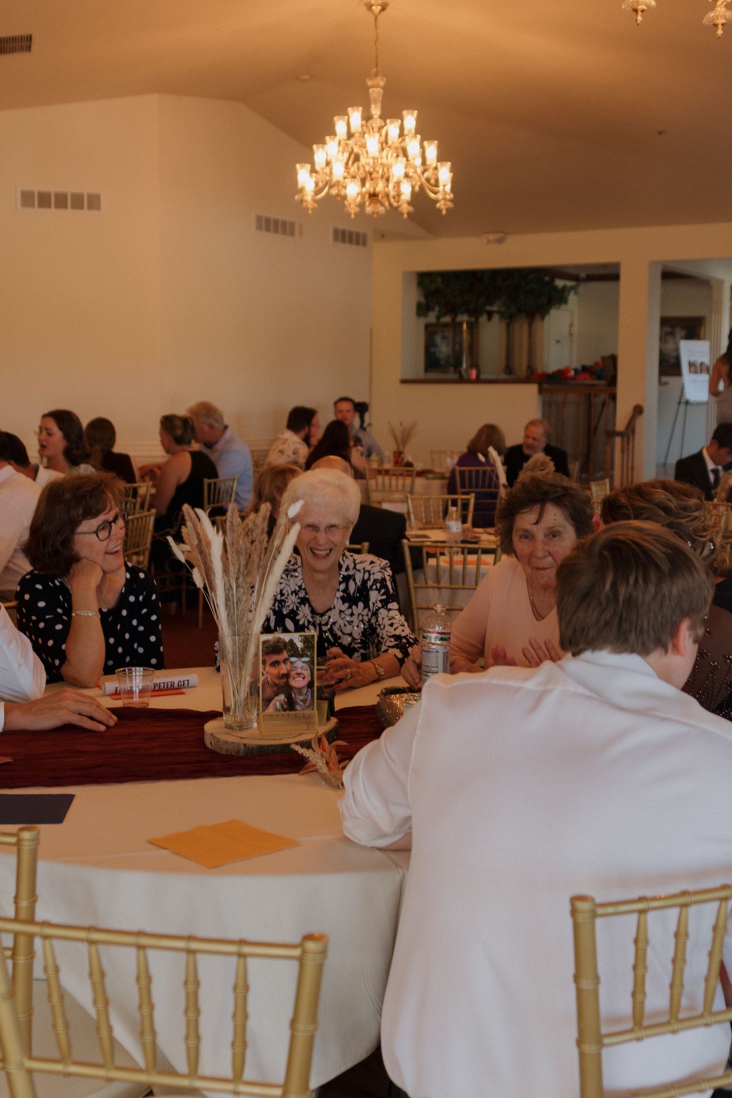 Wedding reception setup with elegant chandeliers and white chiavari chairs in a banquet hall.