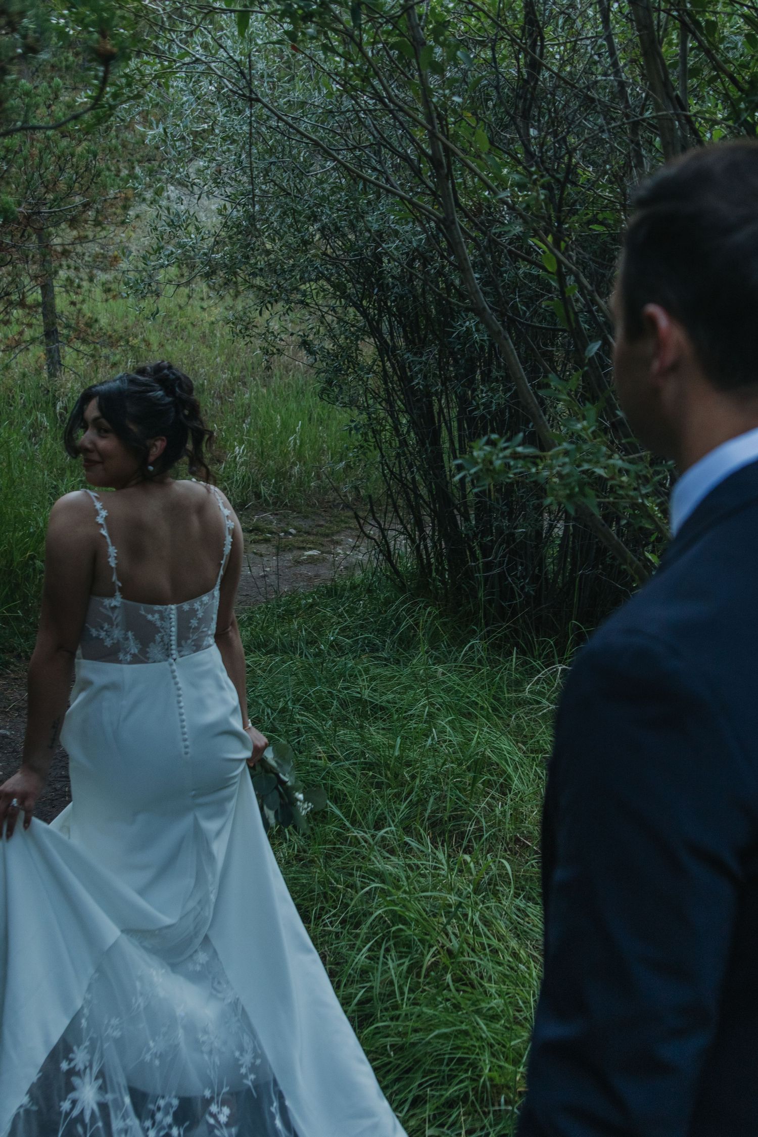 A couple walks through a forest trail, the white wedding dress flowing behind them.