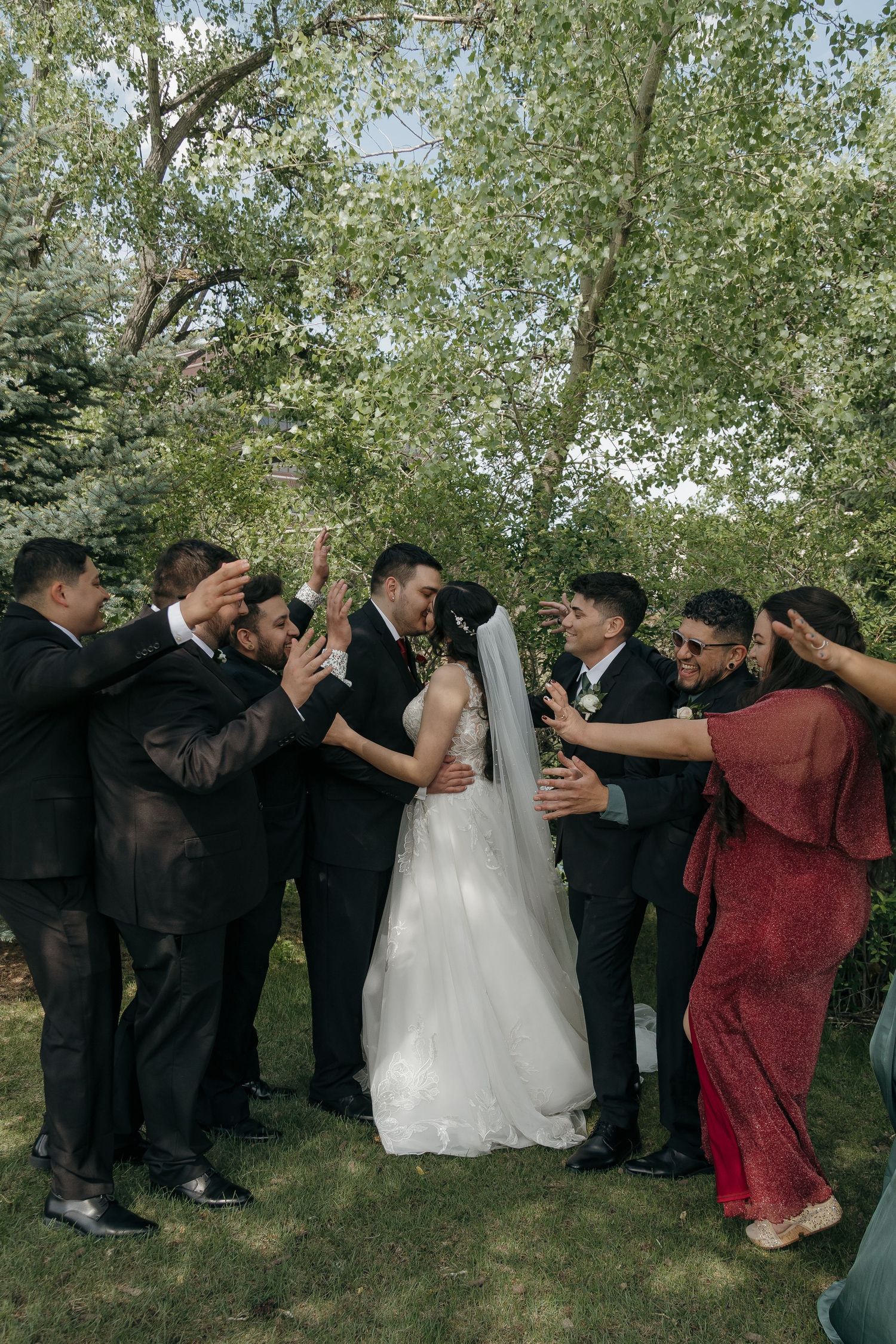 Wedding party celebrating the bride and groom with raised hands and cheers in a lush garden setting.