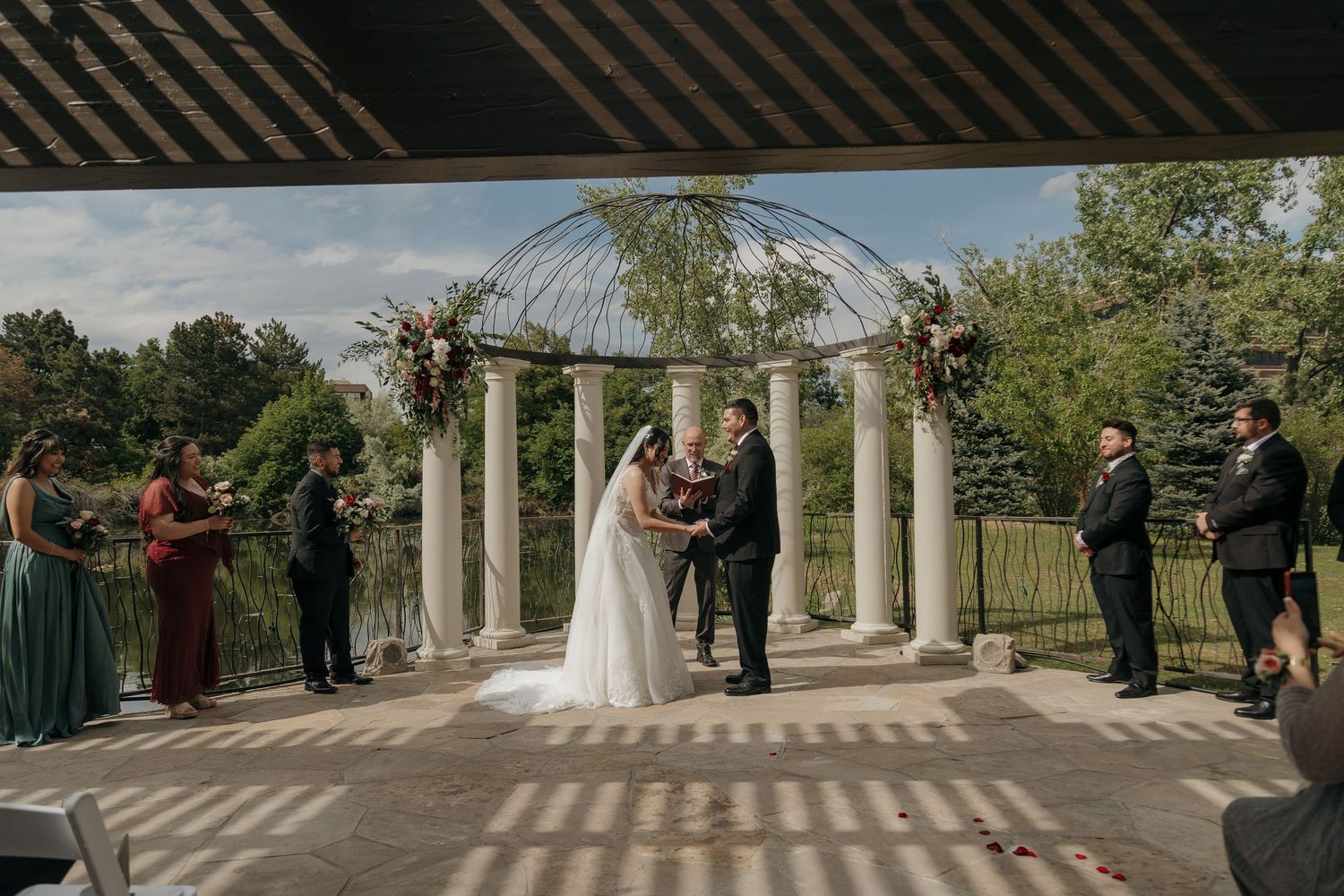 Bride and groom exchanging vows under an elegant outdoor pergola with floral arch and column backdrop.