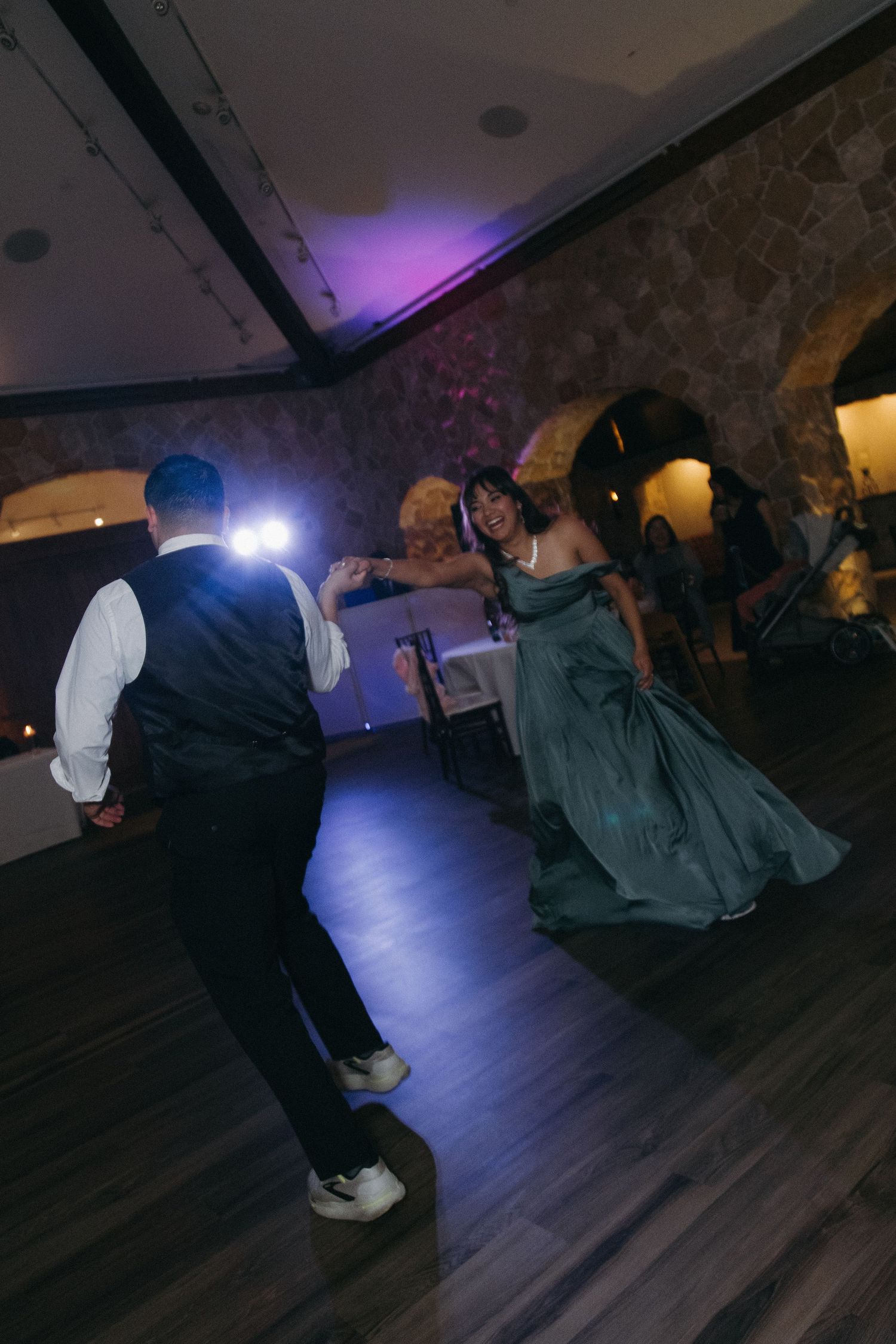 Wedding guests in formal attire dancing energetically on the dance floor at a reception.