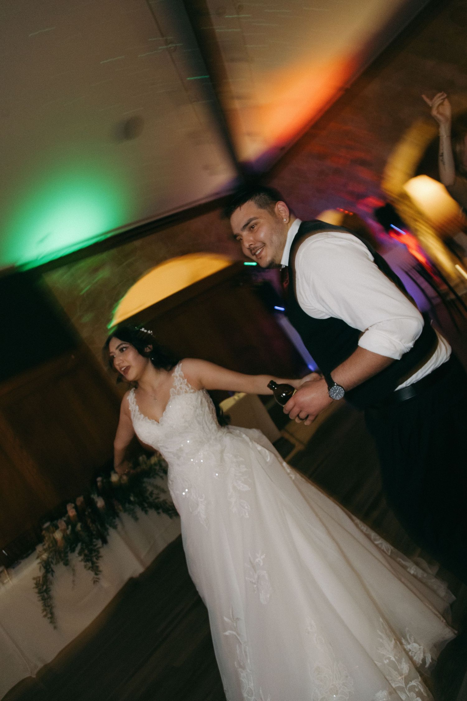 Bride and groom dancing under colorful lights at lively wedding reception.