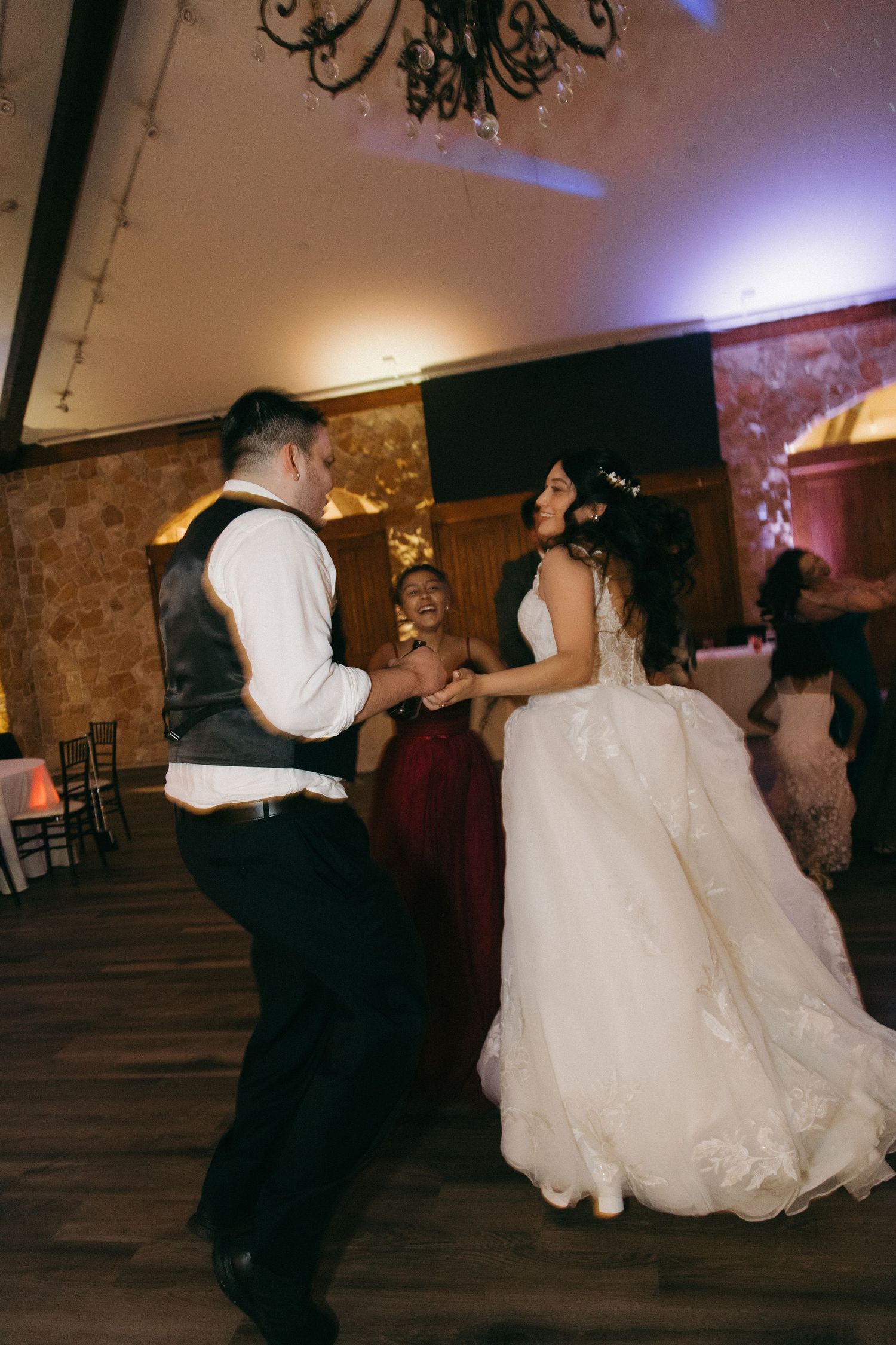 Bride in lace ball gown dances with groom in gray vest during their first dance at wedding reception.
