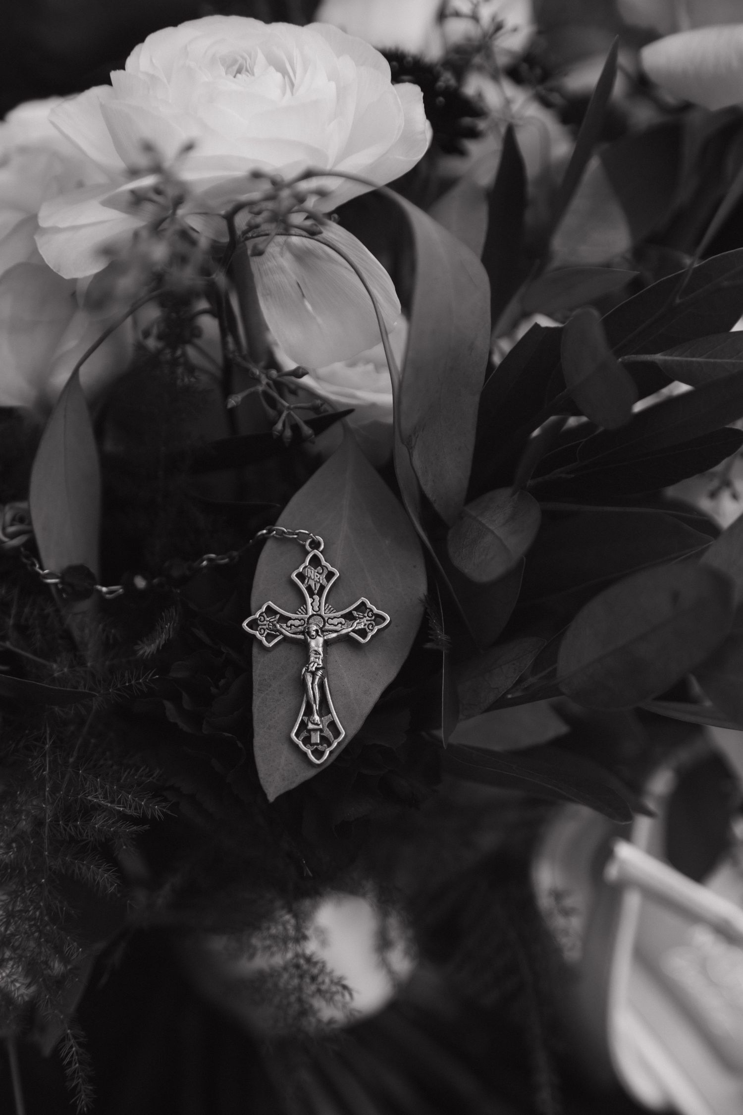 Black and white photo of ornate crucifix cross resting on wedding bouquet.
