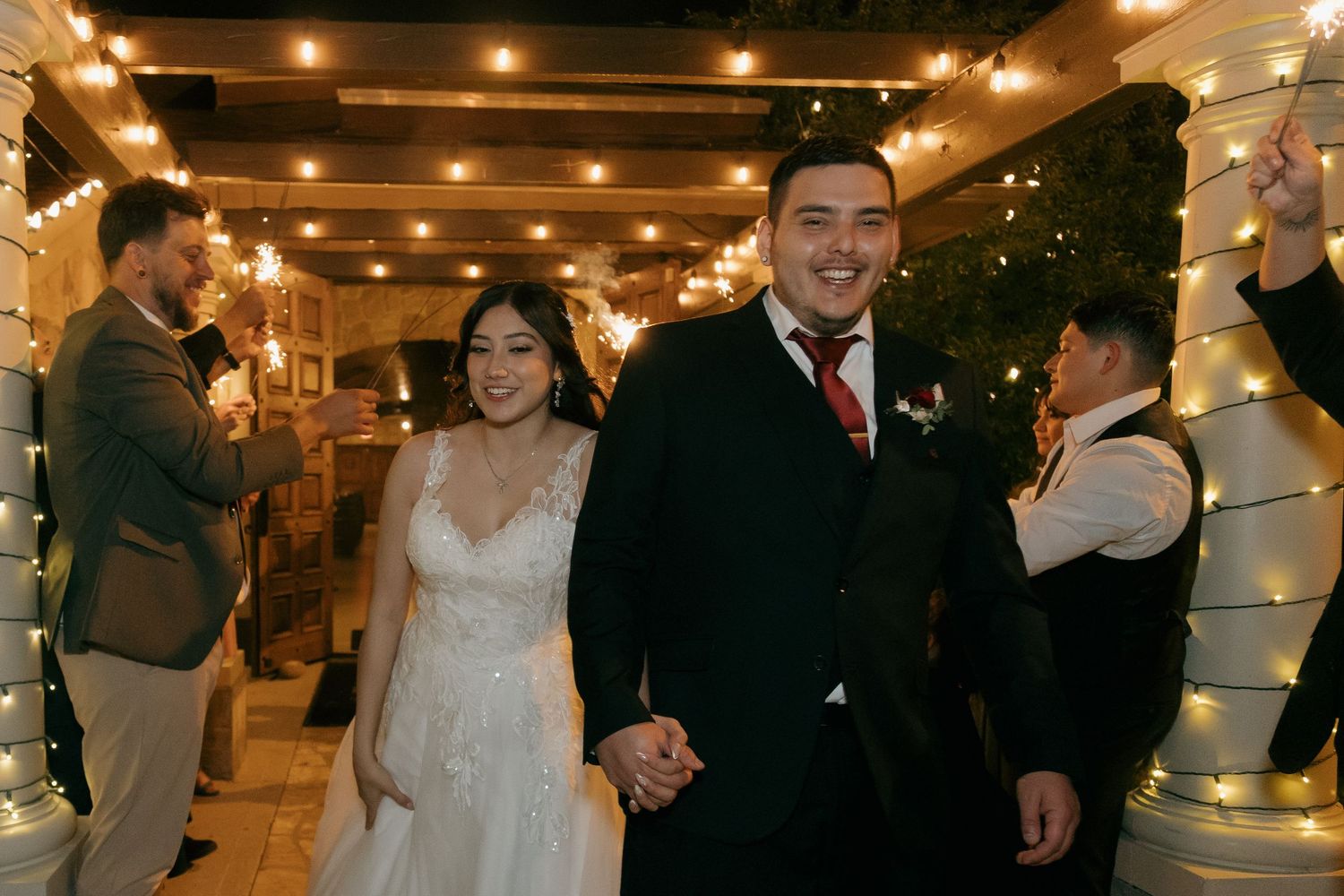Smiling bride and groom walk through sparkler exit at their wedding celebration.