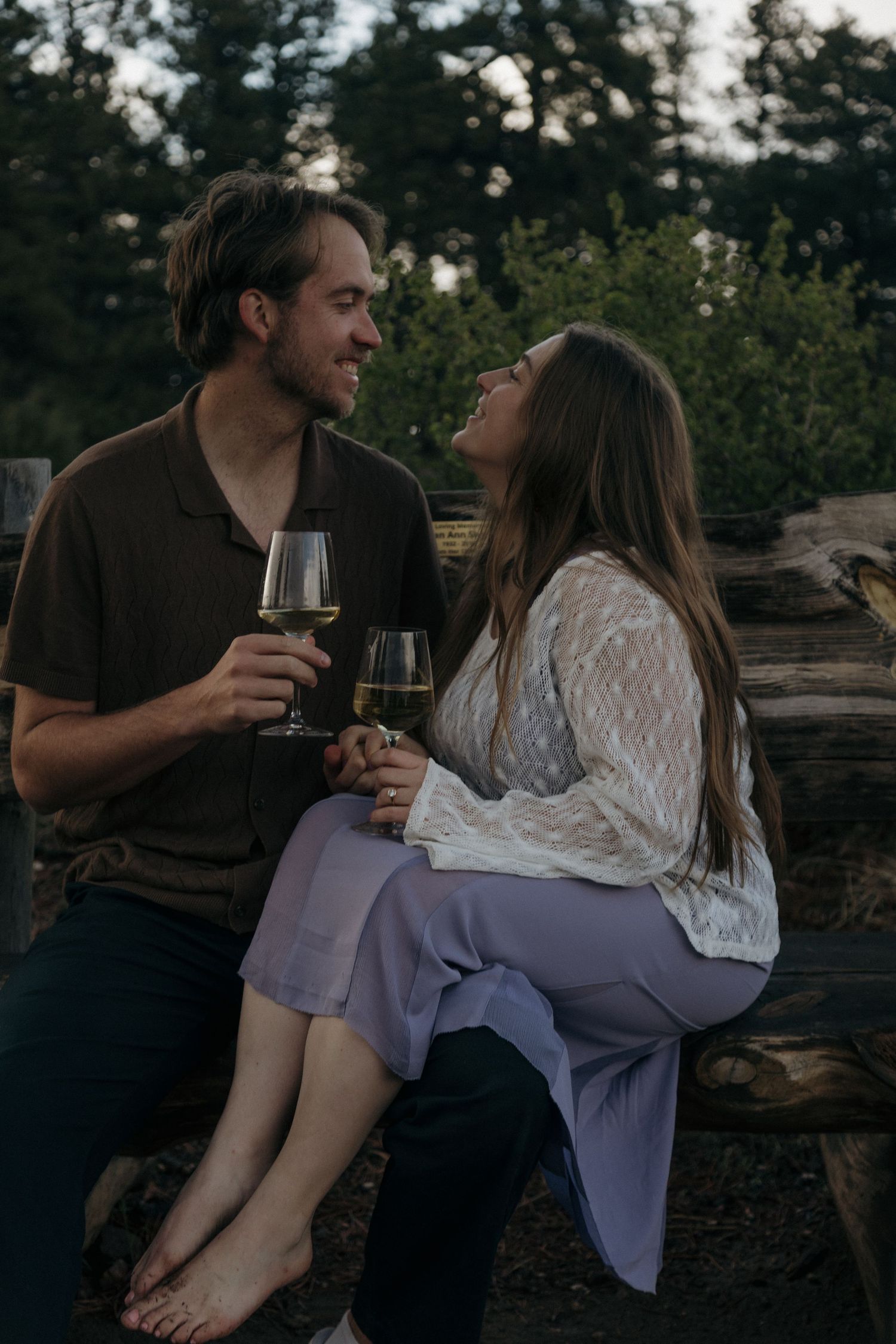 Couple sharing wine glasses and smiling at each other outdoors at dusk.