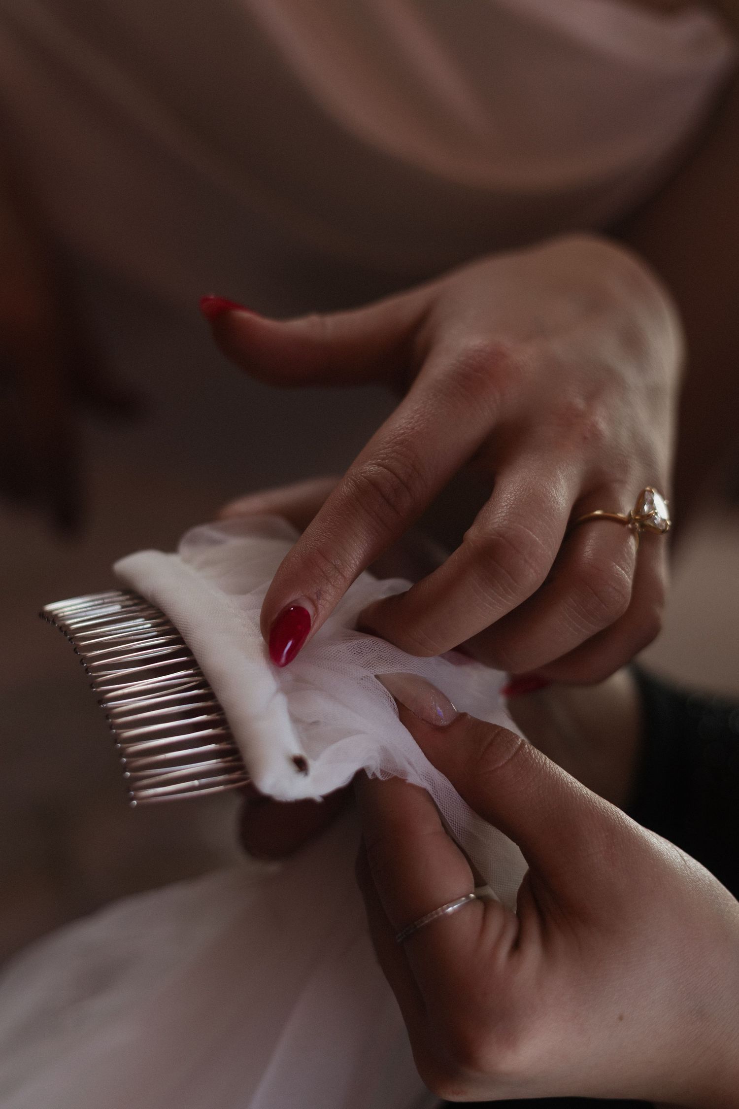 Hands with red nails and an engagement ring adjust a white veil with decorative hair comb.