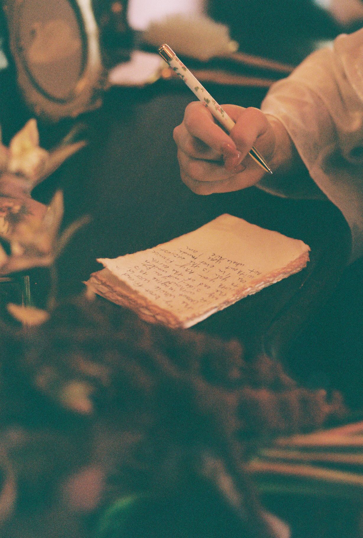 Hands writing personal notes or vows on paper in warm lighting.