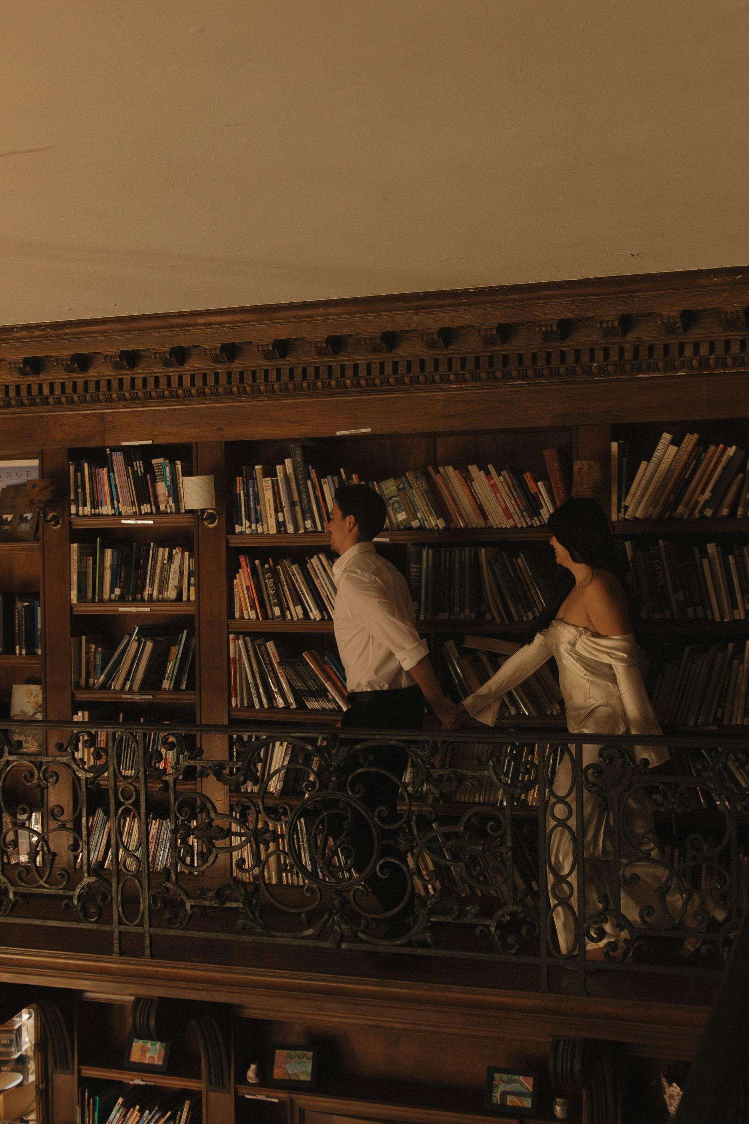 People browsing books in a vintage library with wooden shelves and ornate details.