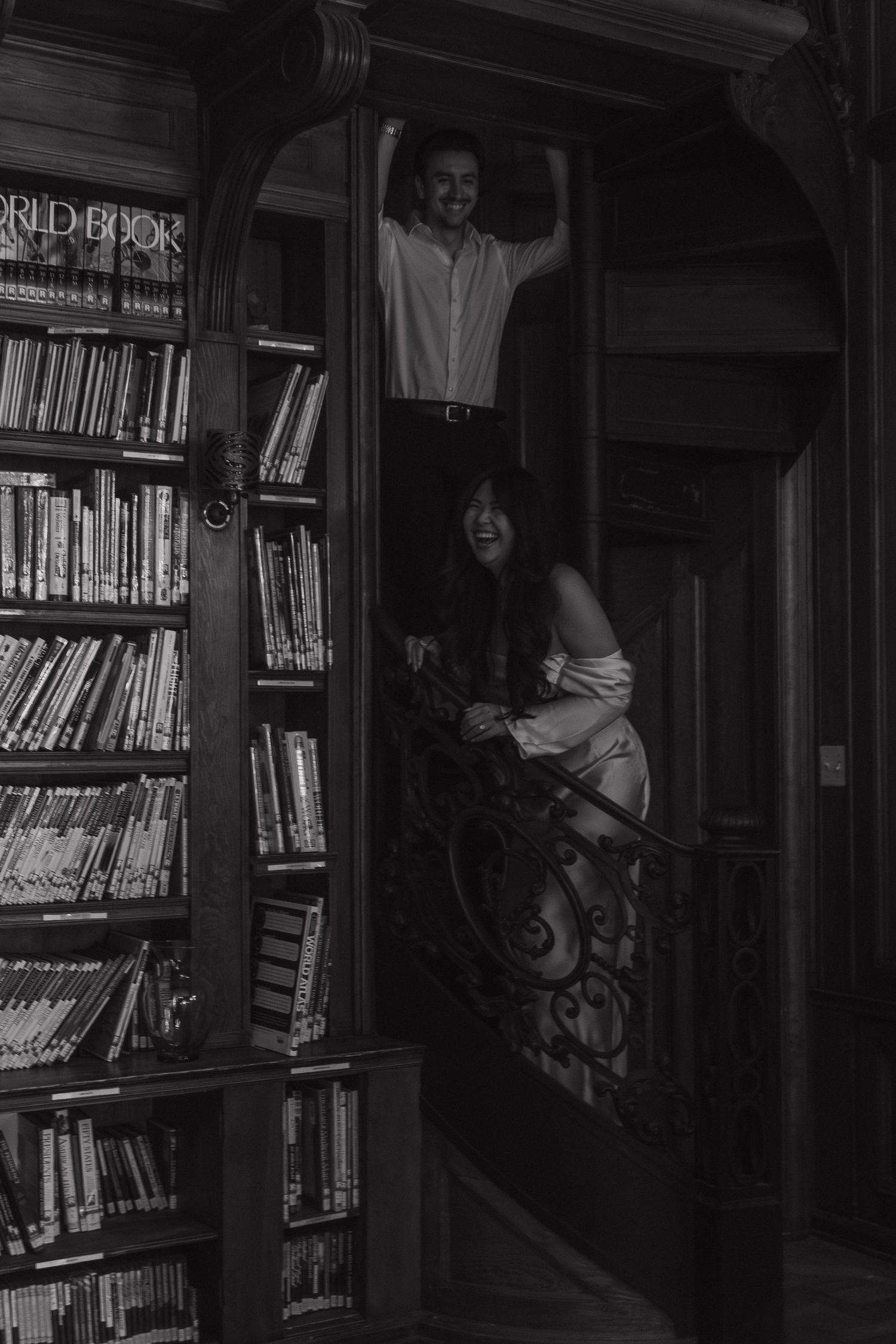 Dark moody photo of figures among library bookshelves with dramatic shadows.
