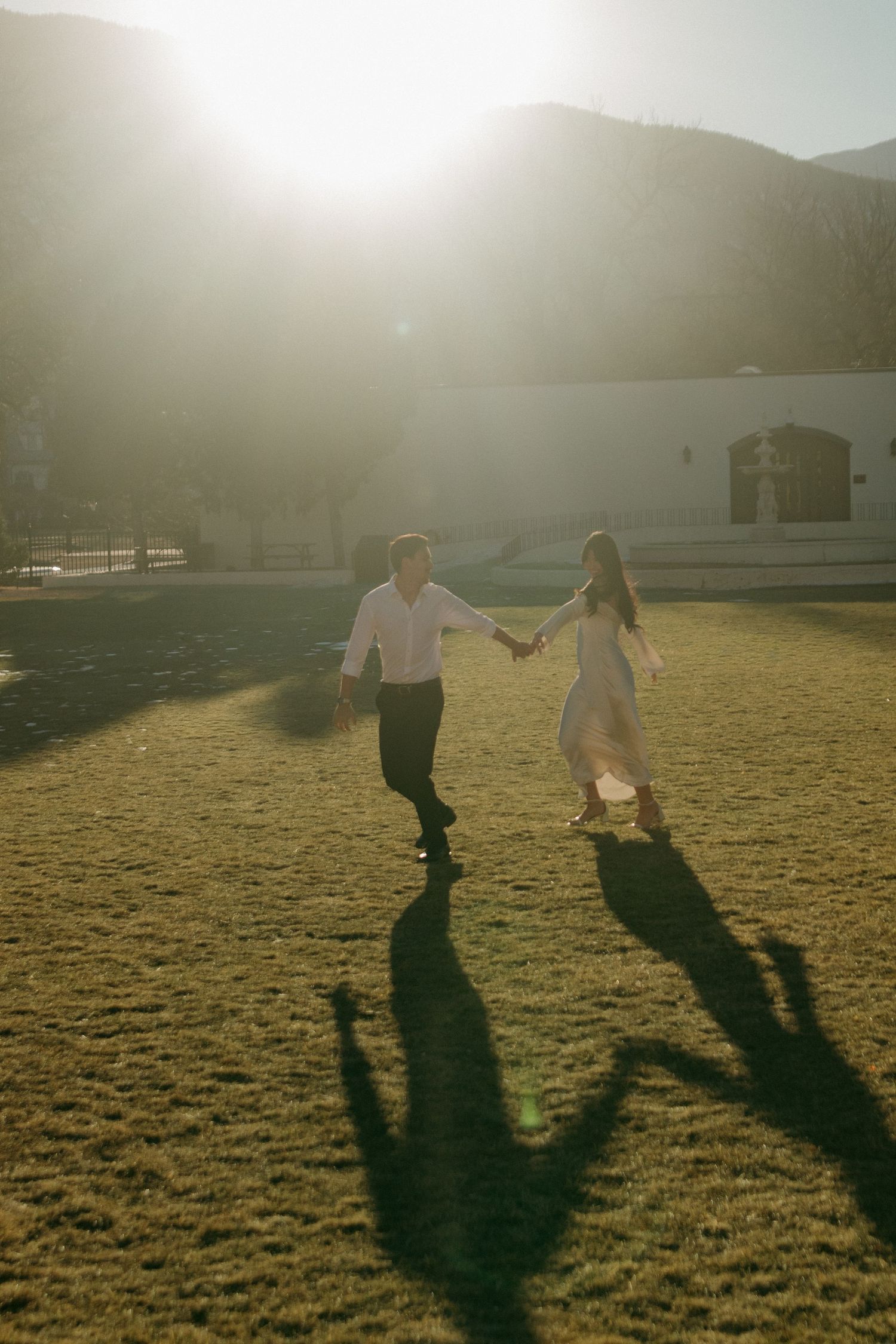 A couple casts long shadows while walking across a sunlit field at sunset.