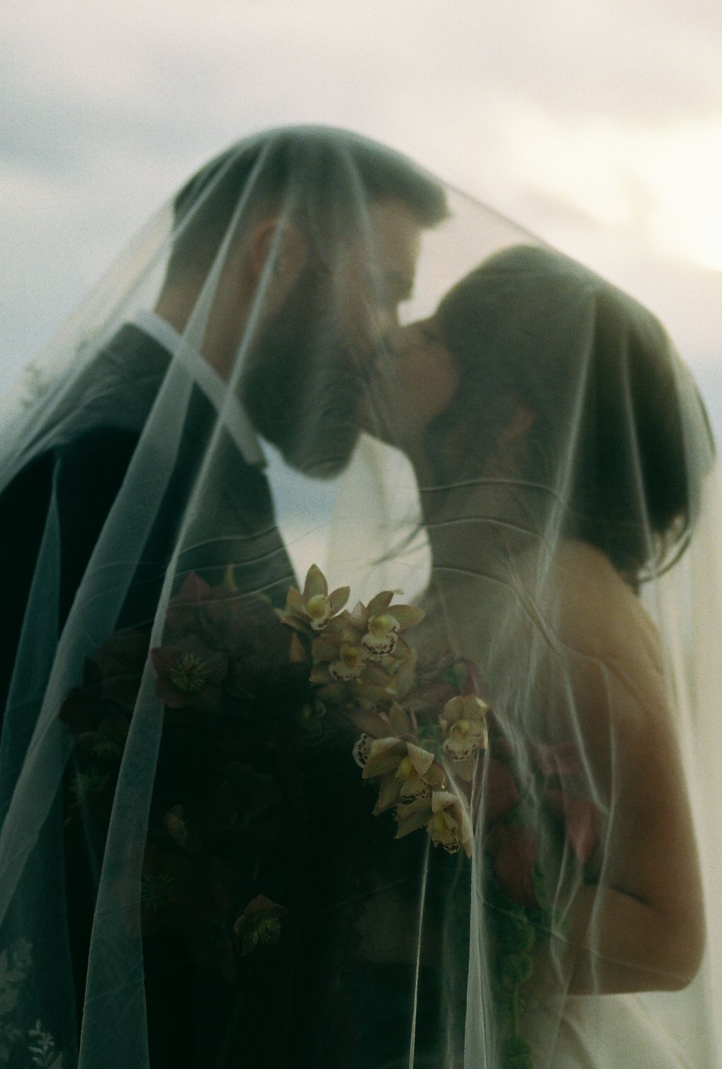 A romantic moment captured through a delicate veil with soft lighting.