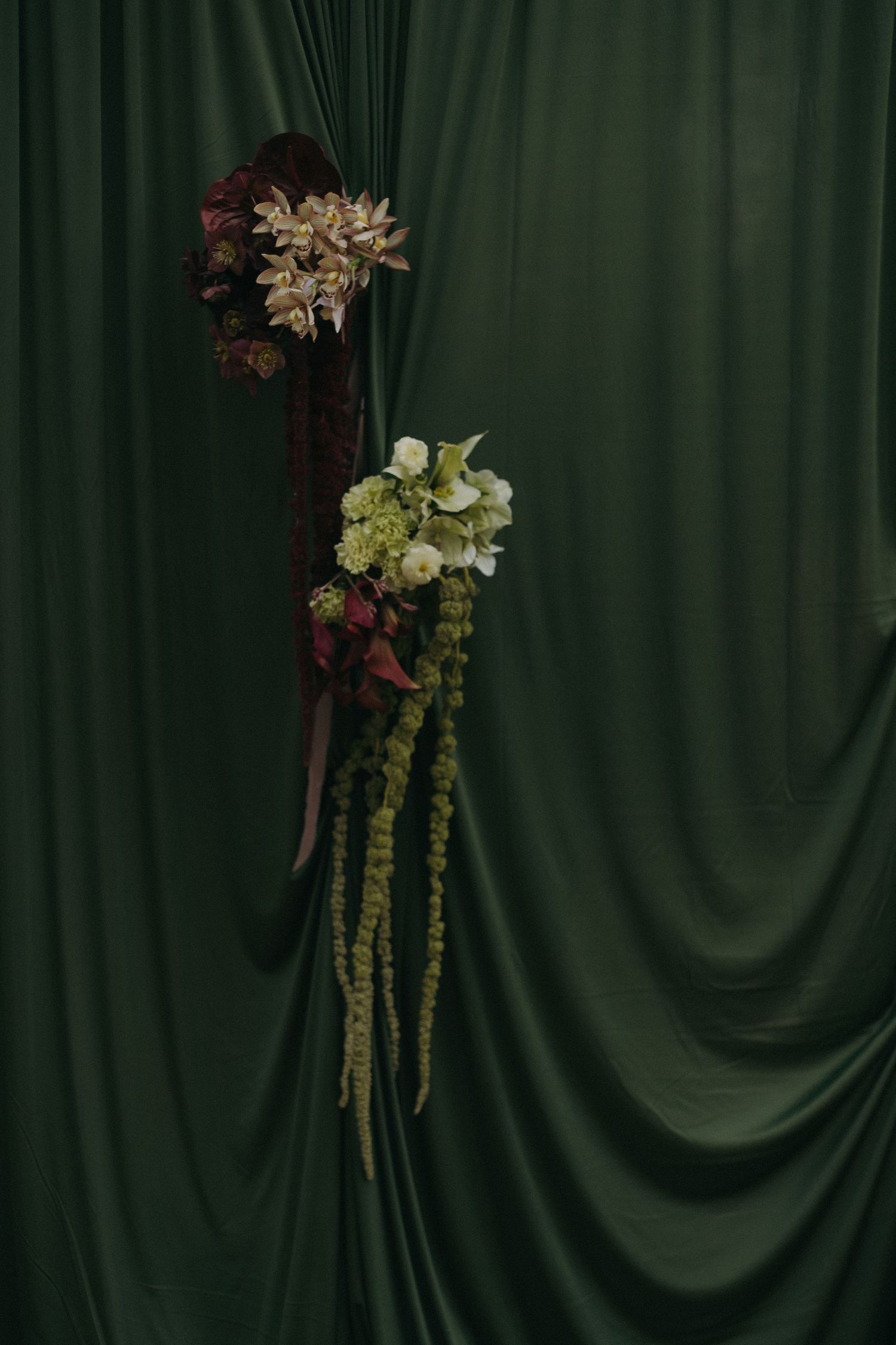 Elegant floral arrangement against a dark green draped backdrop.