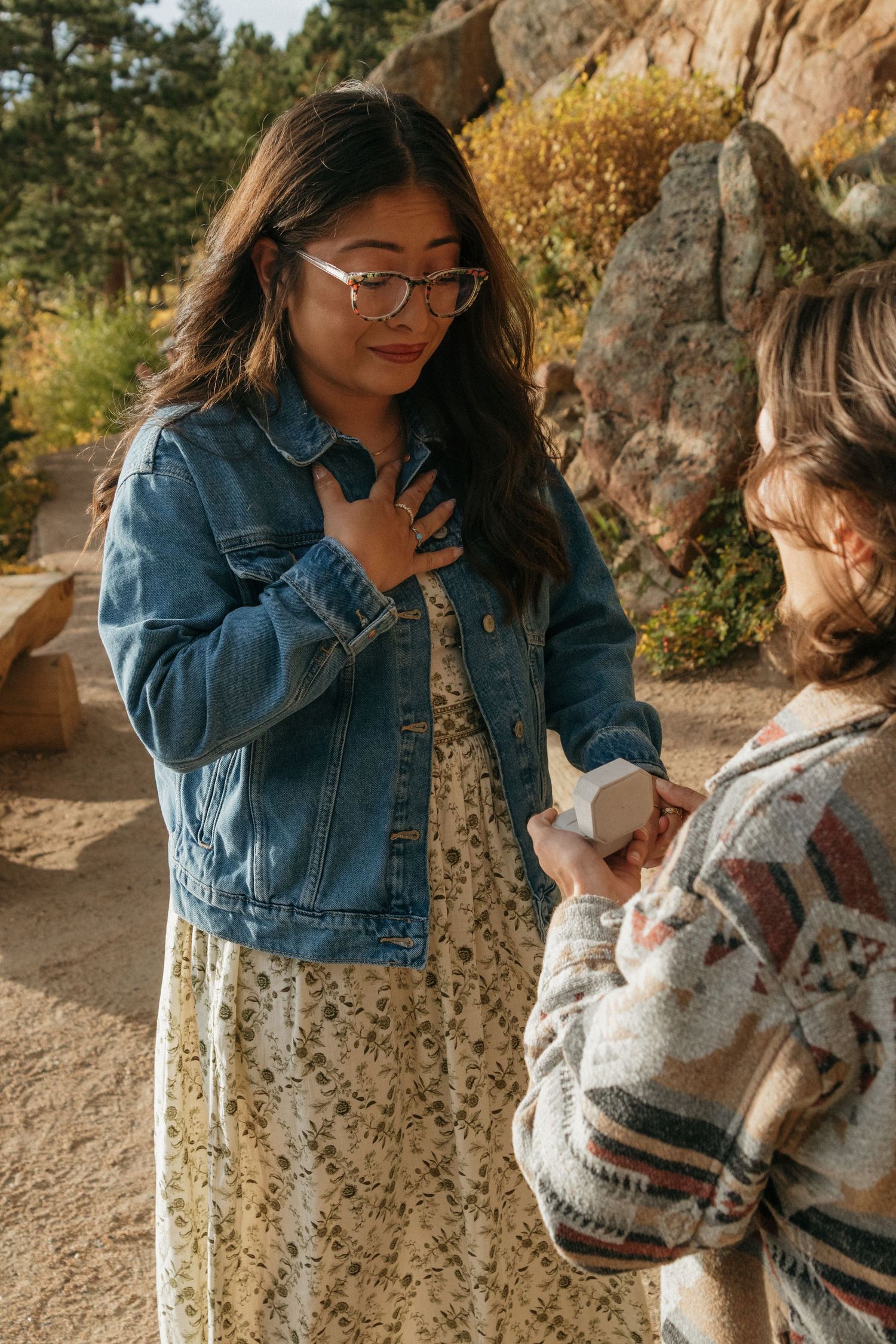 Two people in casual attire share a tender moment against a rocky outdoor backdrop during golden hour.
