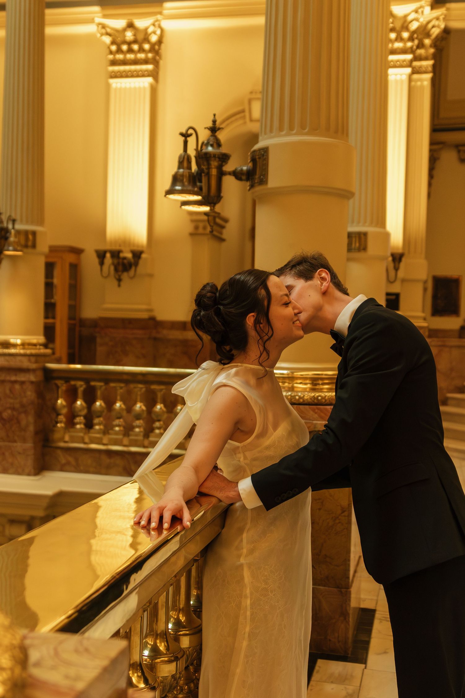 Romantic moment between newlyweds along an elegant marble railing with classical columns.