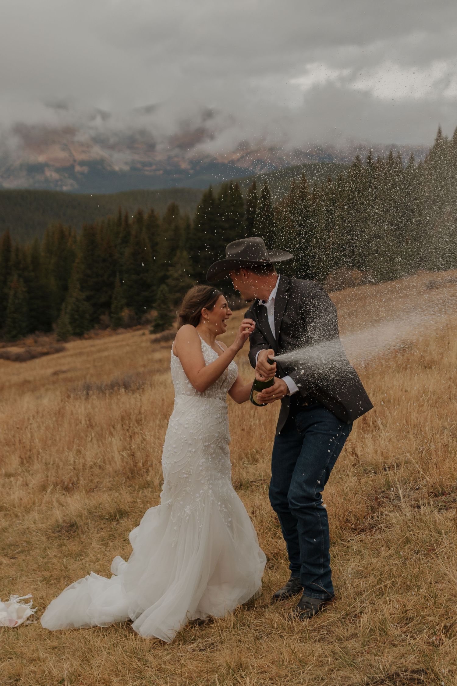 Newlyweds celebrate with champagne spray in a mountain meadow.