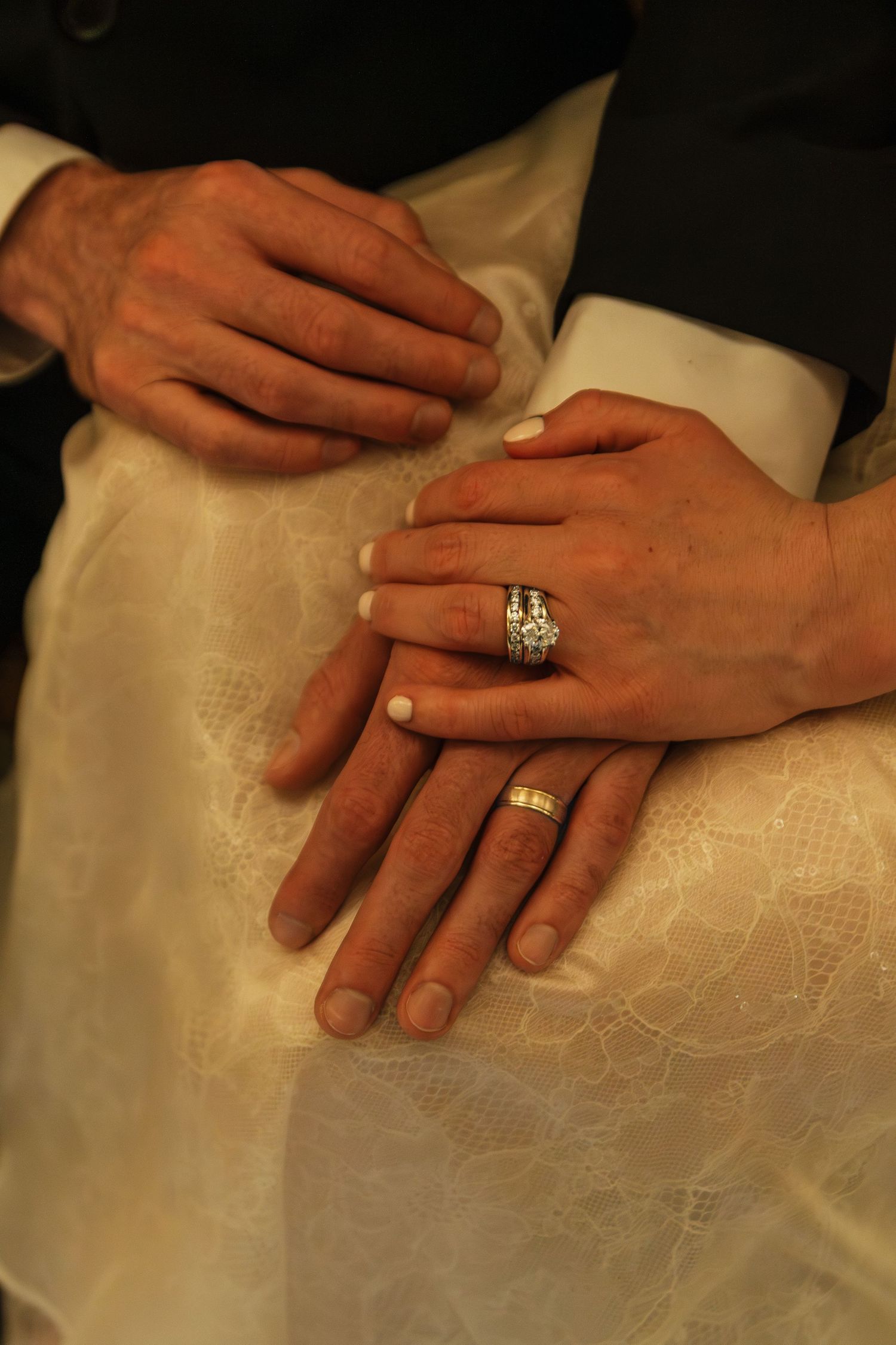 Wedding rings and hands photographed against white fabric in warm lighting.