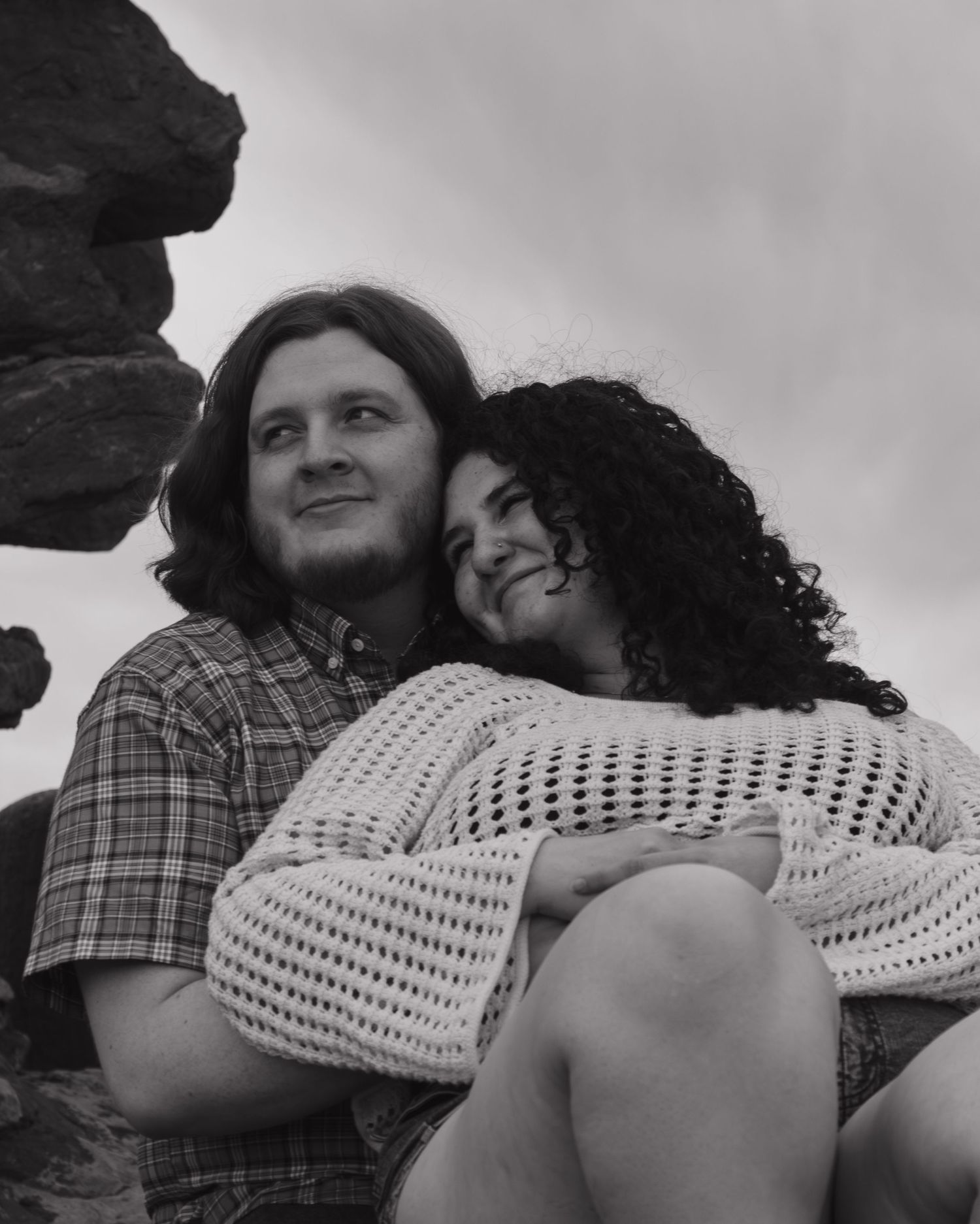 Black and white intimate portrait captured against cloudy skies and rock formations.