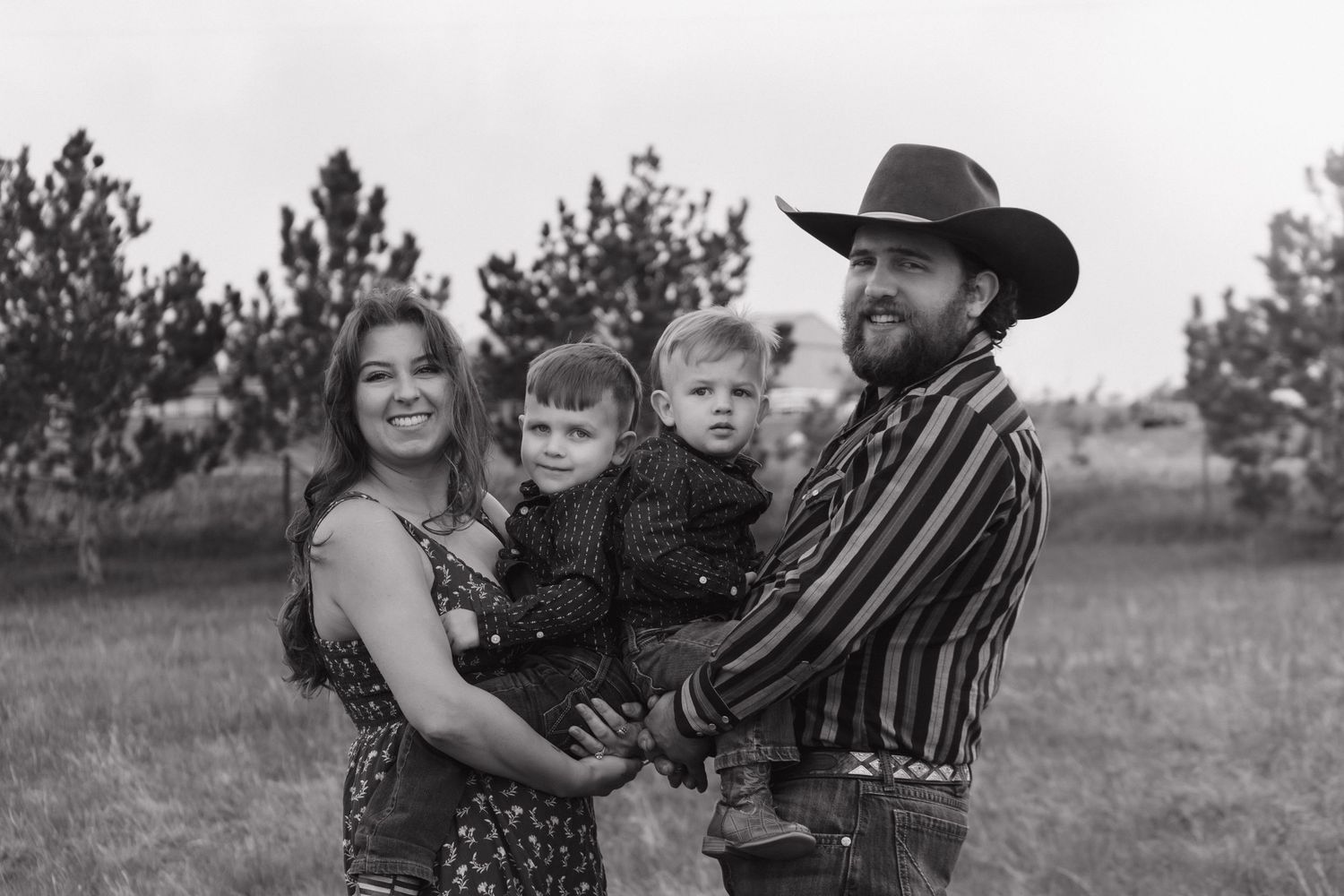Black and white outdoor family portrait with a cowboy hat and striped shirt against a rural backdrop.