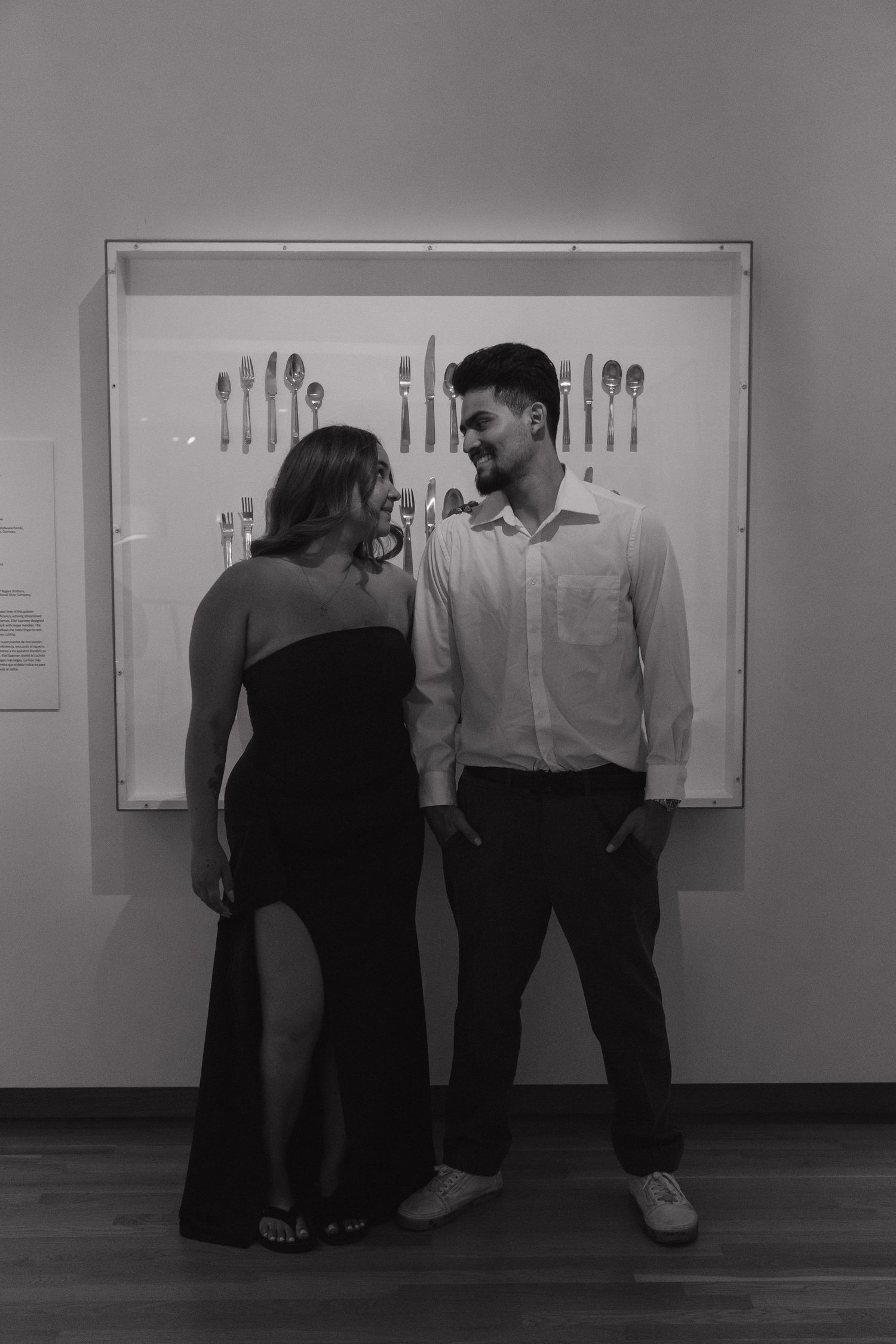 Black and white photo of a smiling couple standing together in a museum in front of a silverware display case.