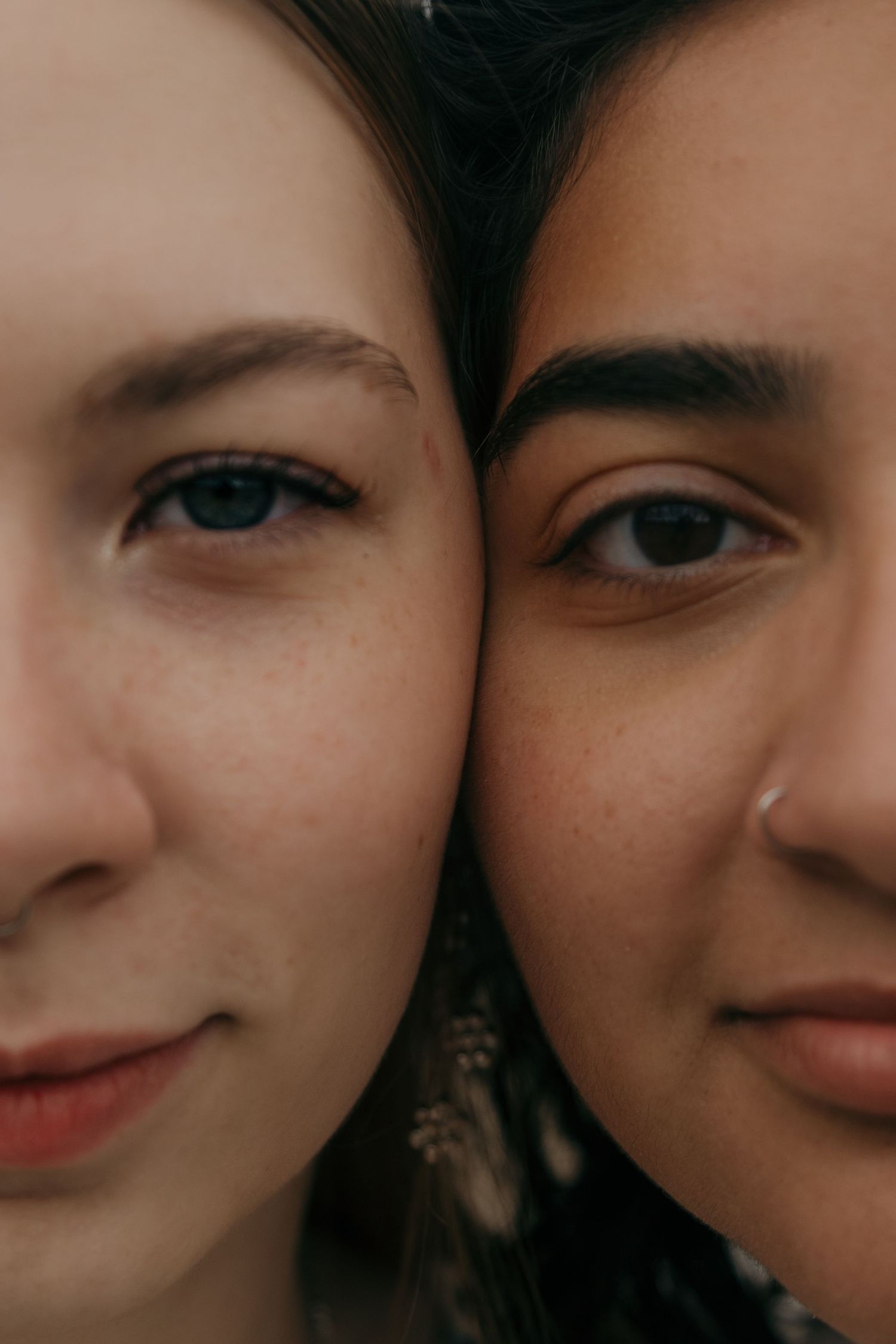 Intimate close-up portrait of two women with faces pressed together, showing half of each face.
