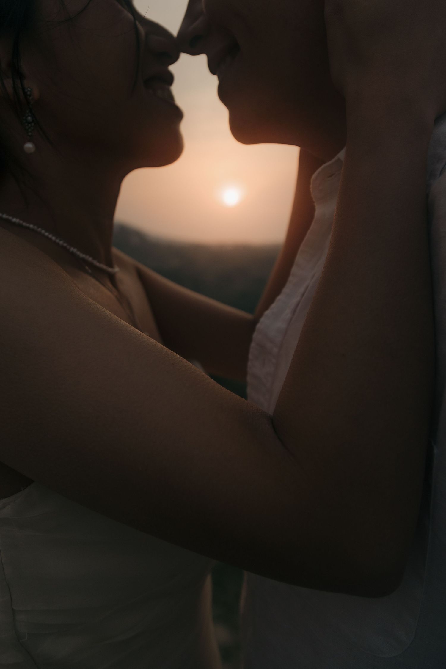 Silhouette of couple nearly kissing framed by a golden sunset over mountain landscape.