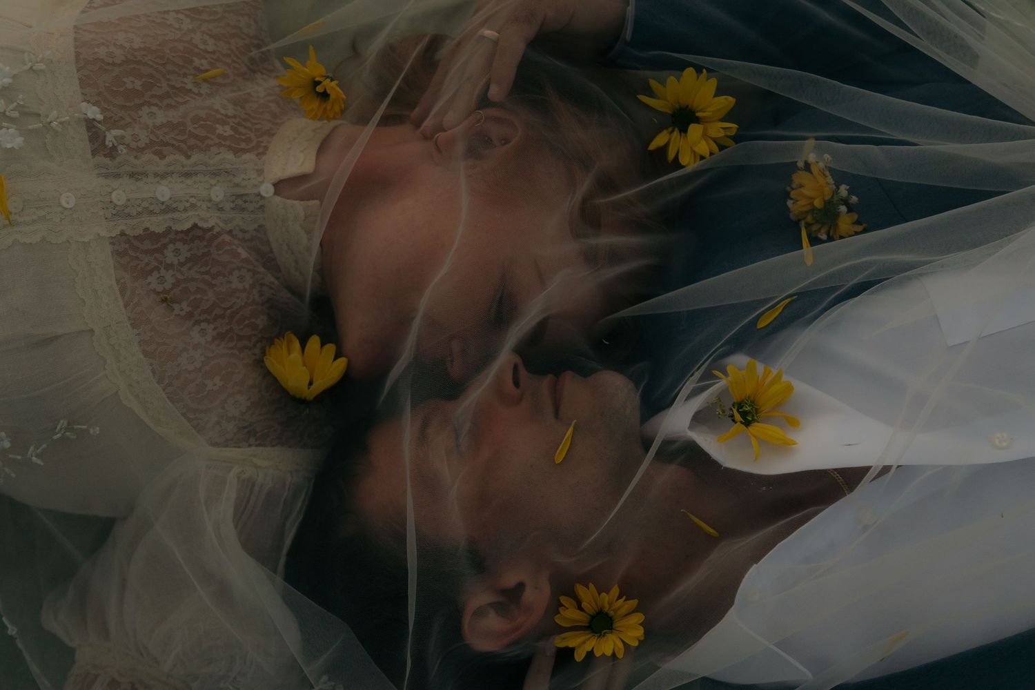 Romantic overhead view of bride and groom kissing under veil adorned with yellow sunflowers.
