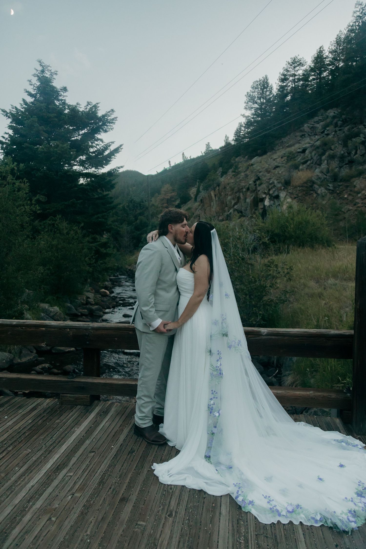 Bride and groom share a kiss on a wooden bridge with mountain canyon backdrop during their elopement.