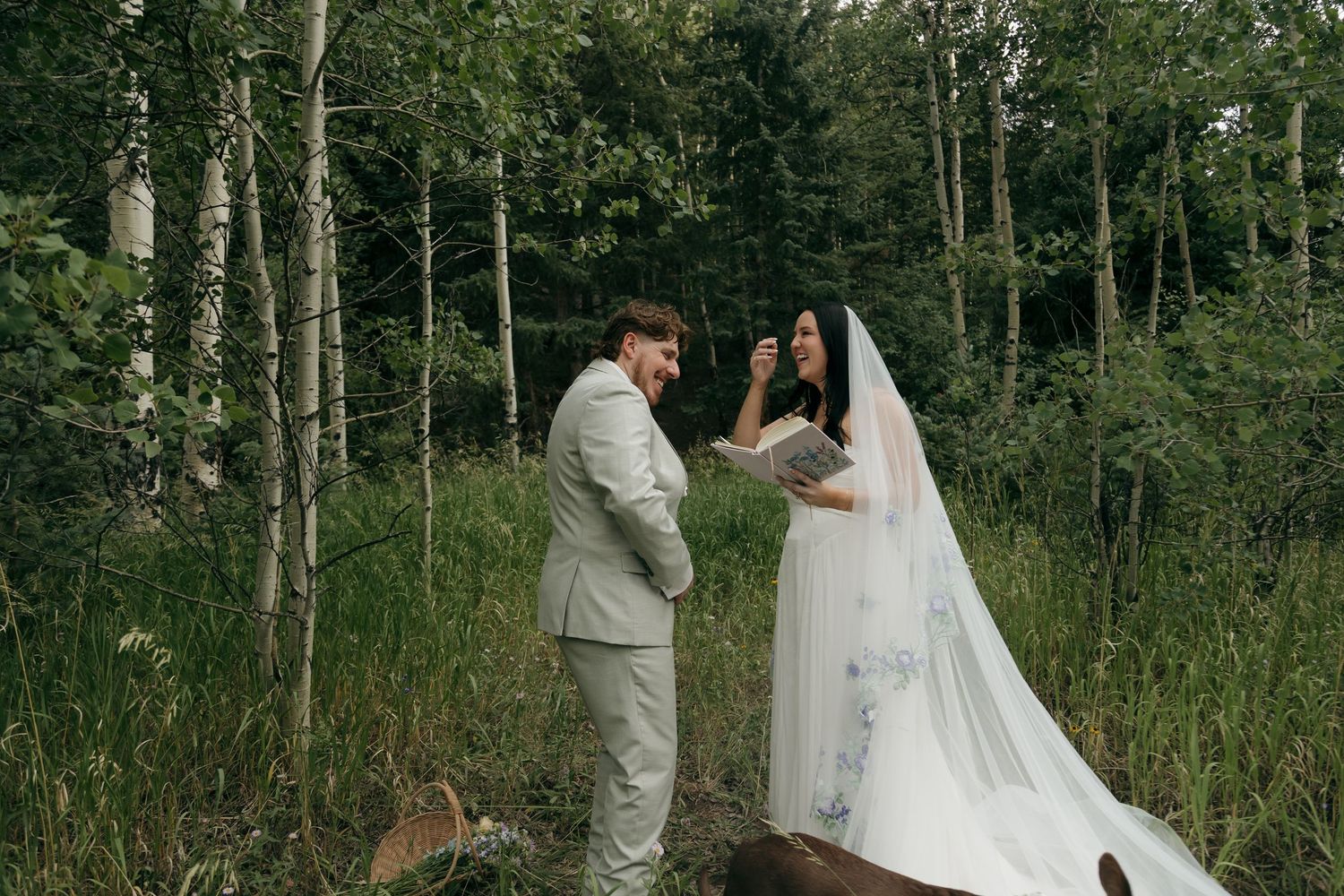 Groom reads vows to bride in a serene forest setting, bride wearing a painted floral veil.