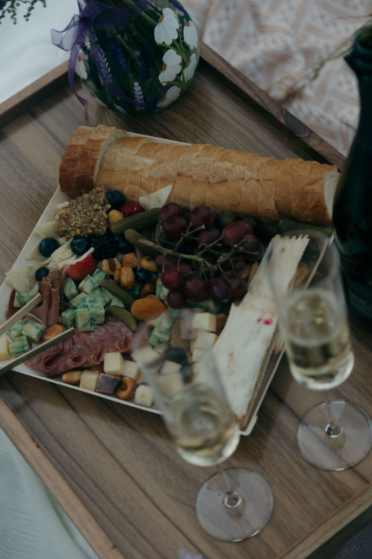Elegant wedding charcuterie board with baguette, grapes, meats, cheeses beside champagne glasses.