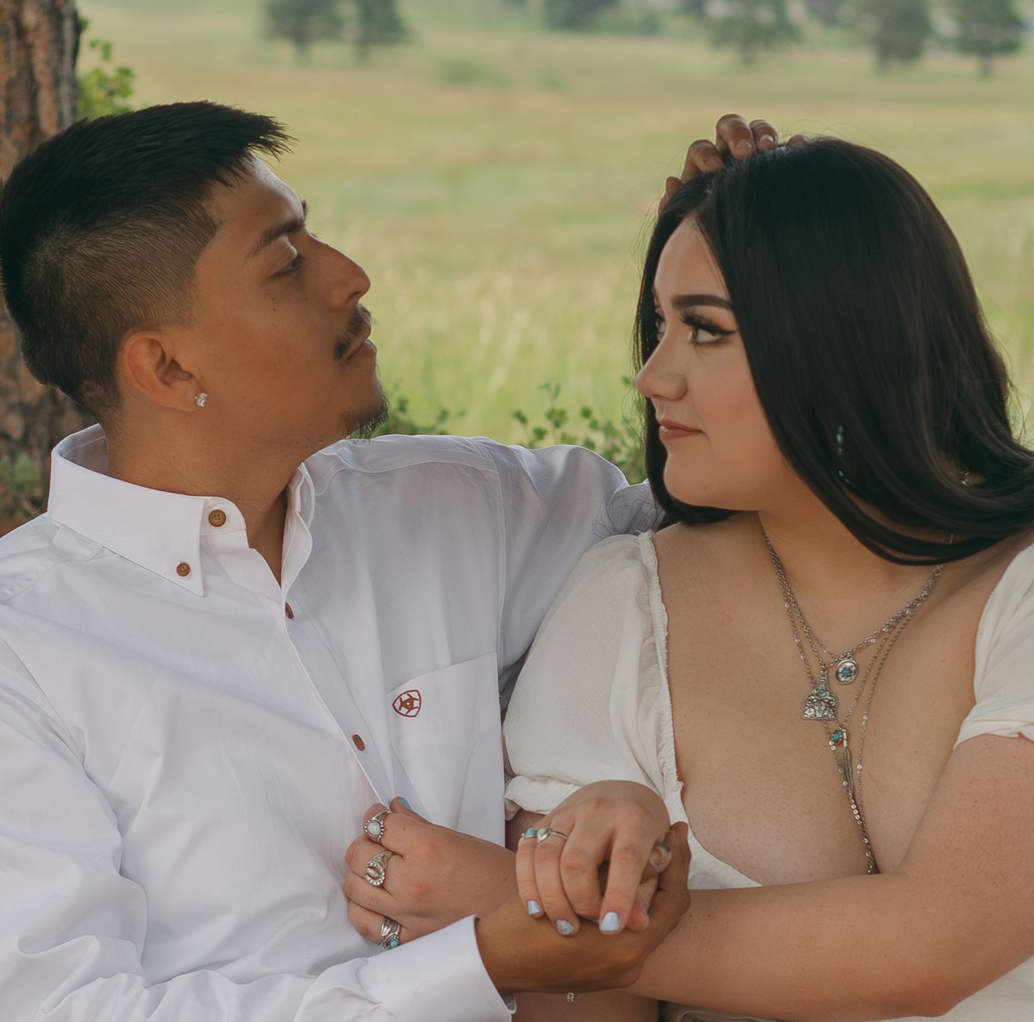 Close-up of couple in white shirts sharing tender moments in natural outdoor setting.