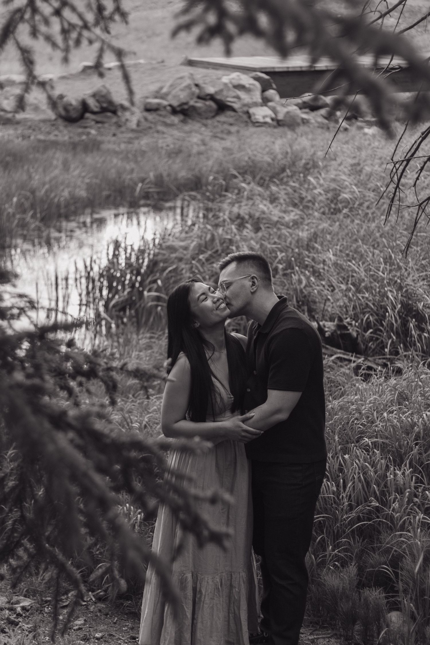 A romantic black and white portrait by a pond with trees framing the scene.