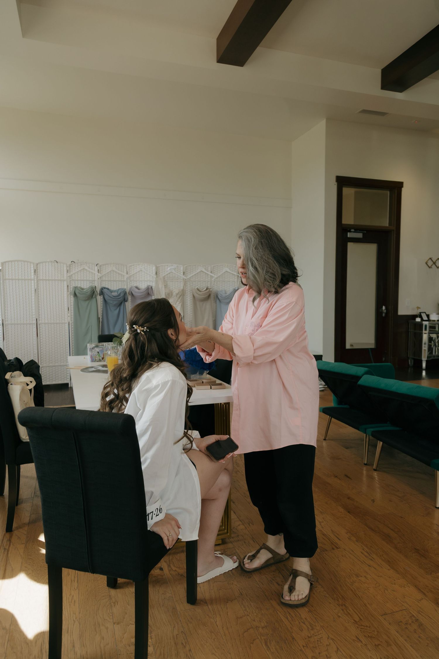 Older woman helping bride with hair and makeup preparations in a bright bridal suite before the wedding.
