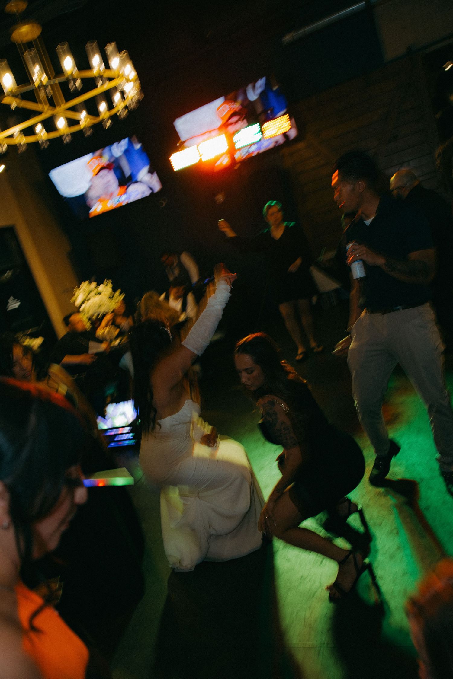 Bride and wedding guests dance under colorful lights at lively reception party.