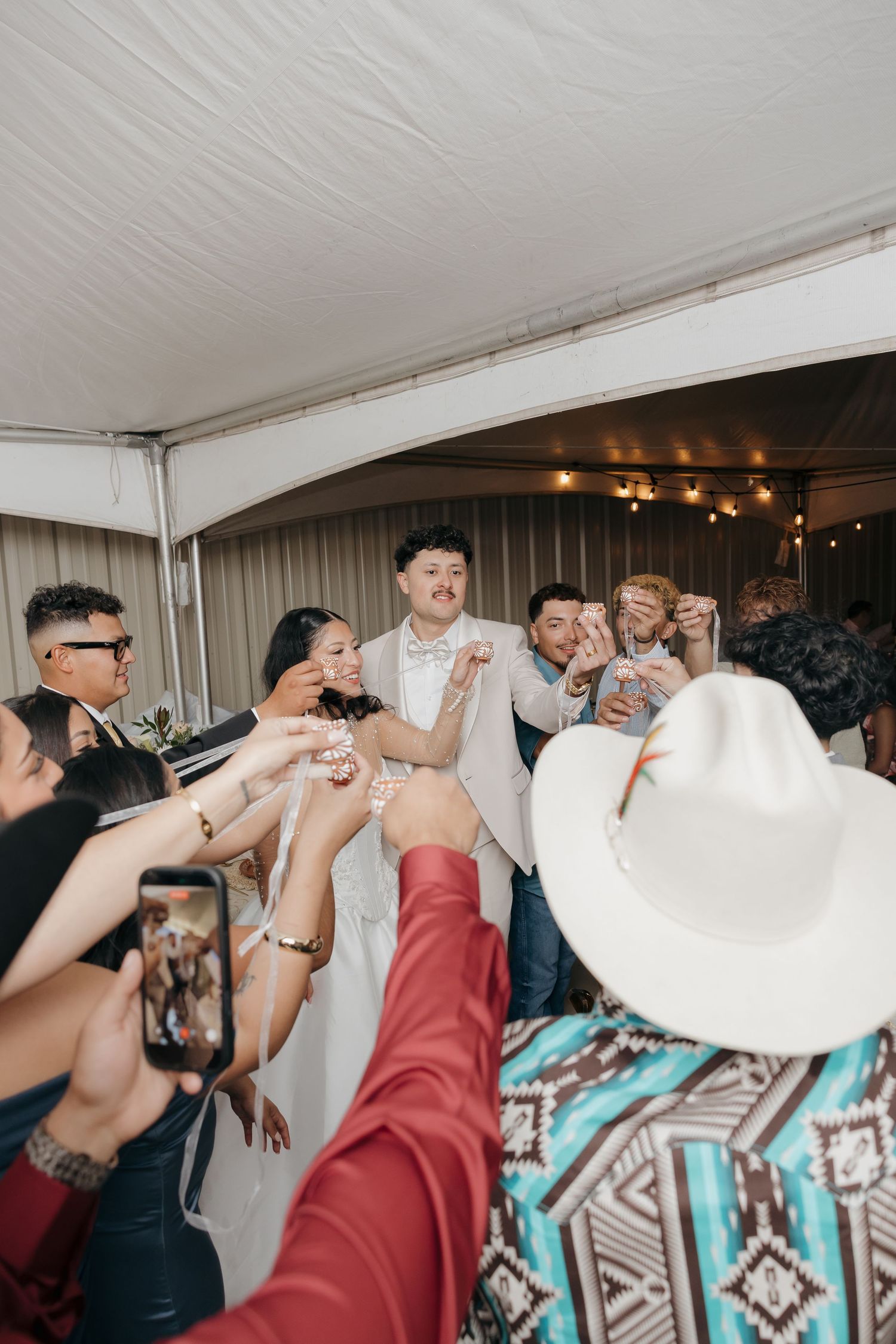 Bride and groom celebrated by cheering guests at lively indoor wedding reception dance floor.
