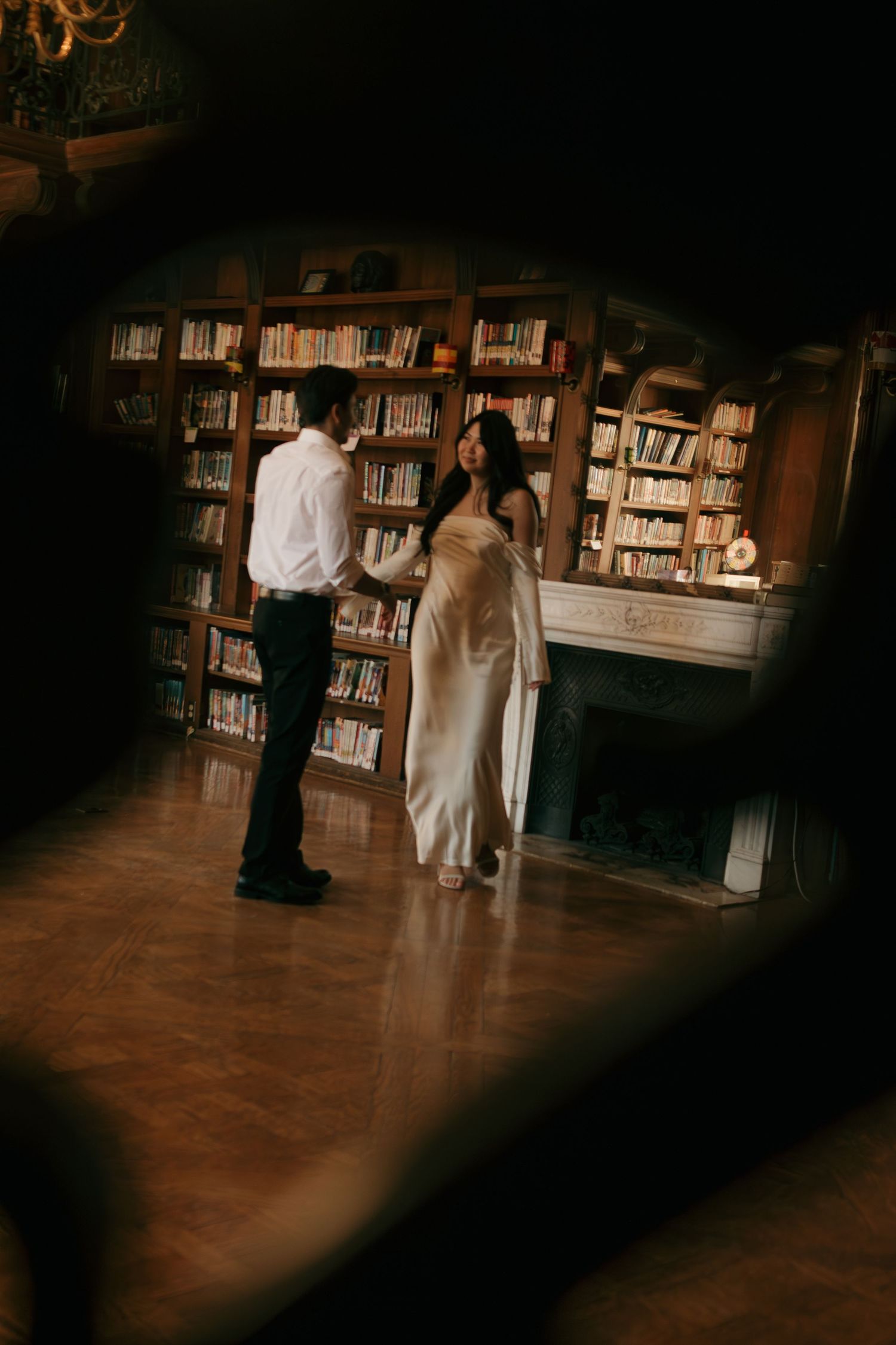 A dimly lit library interior with bookshelves and figures moving through the space.