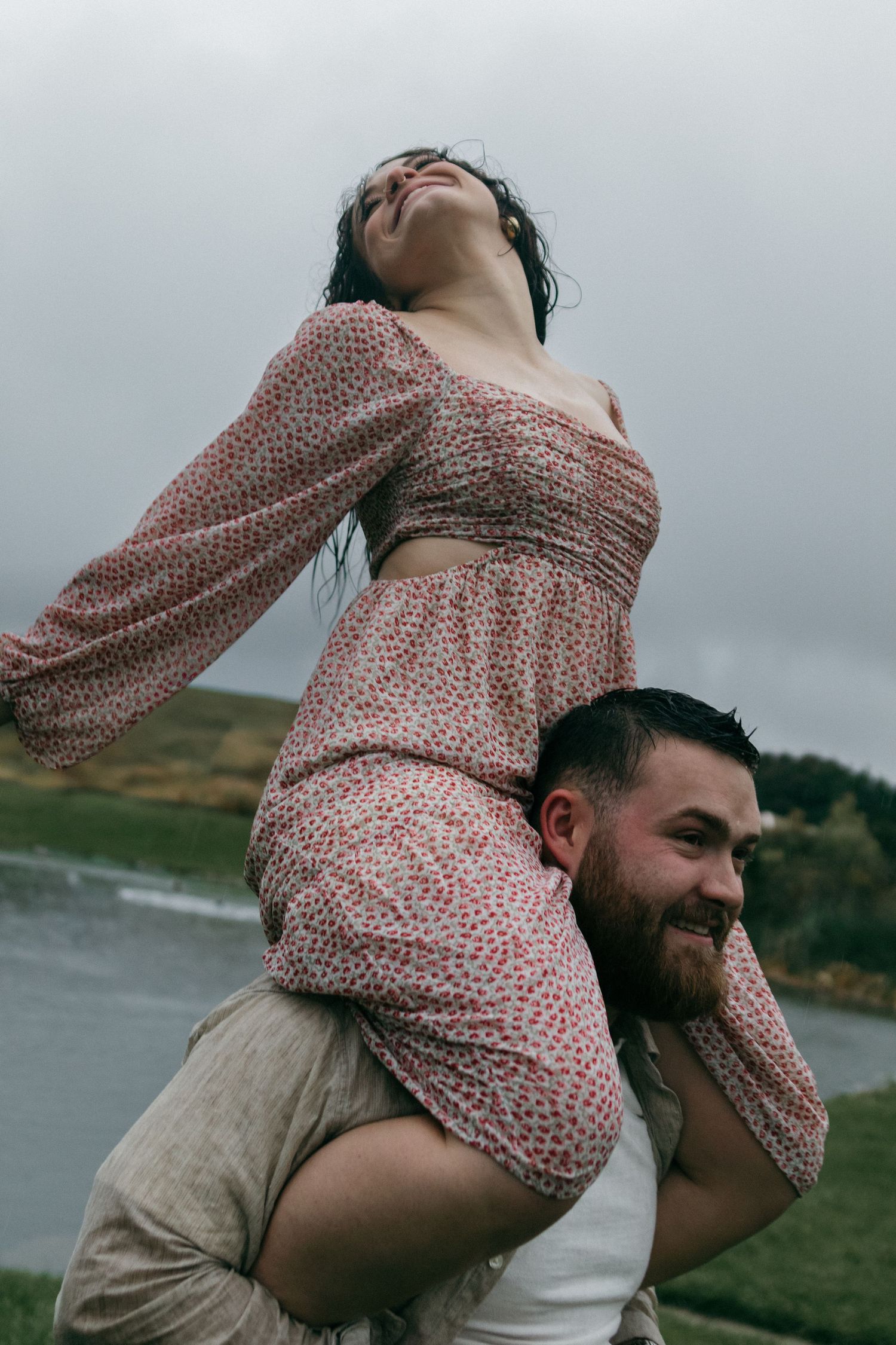 A playful couple shares a joyful moment as she sits on his shoulders in a floral dress.